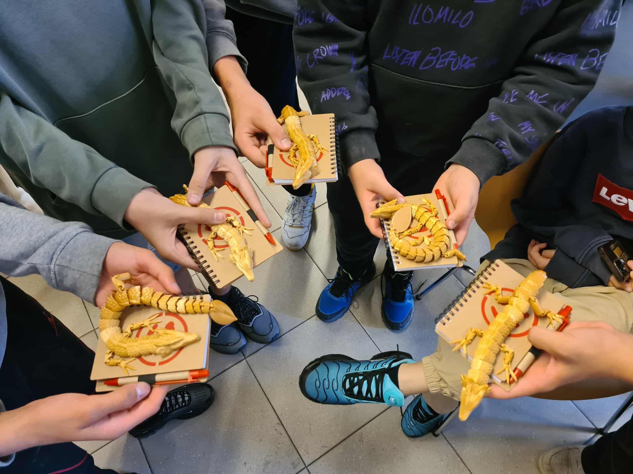 Kilku uczestników turnieju trzyma w dłoniach złote smoki wydrukowane w 3D oraz notesy z logo NASTKI — nagrody za udział w turnieju Brawl Stars.