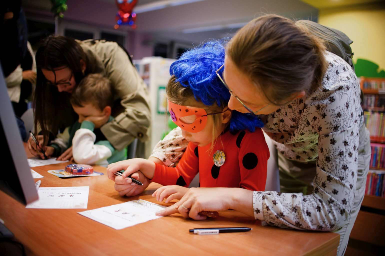 Dzieci w przebraniach rozwiązują zadania przy stoliku z pomocą dorosłych.