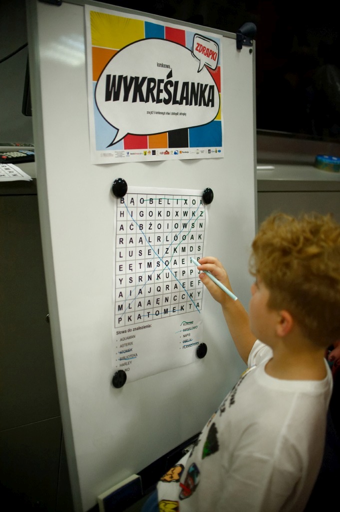 Chłopiec rozwiązuje komiksową wykreślankę na tablicy.