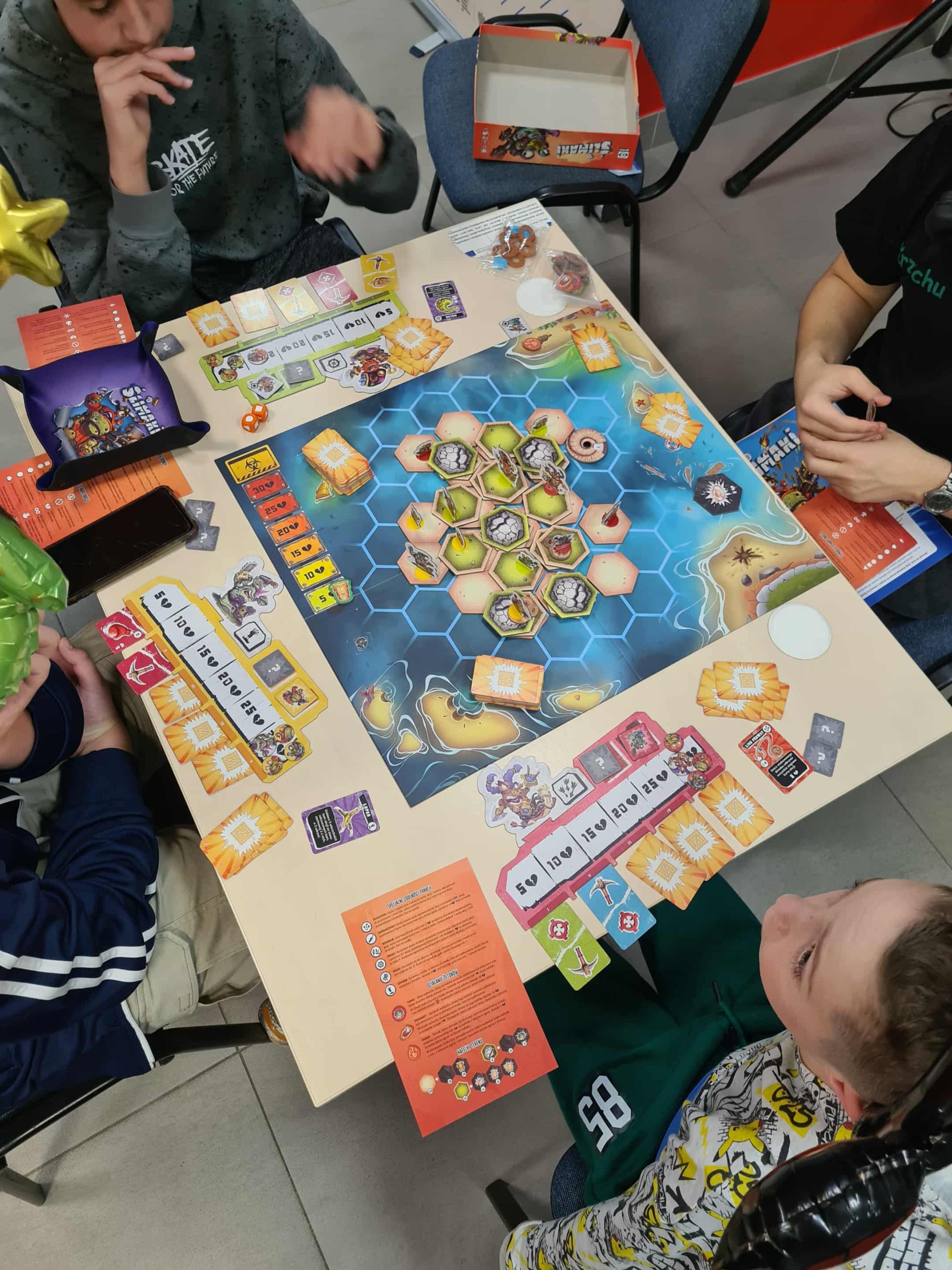 Grupa chłopców gra w kolorową grę planszową z heksagonalną planszą.