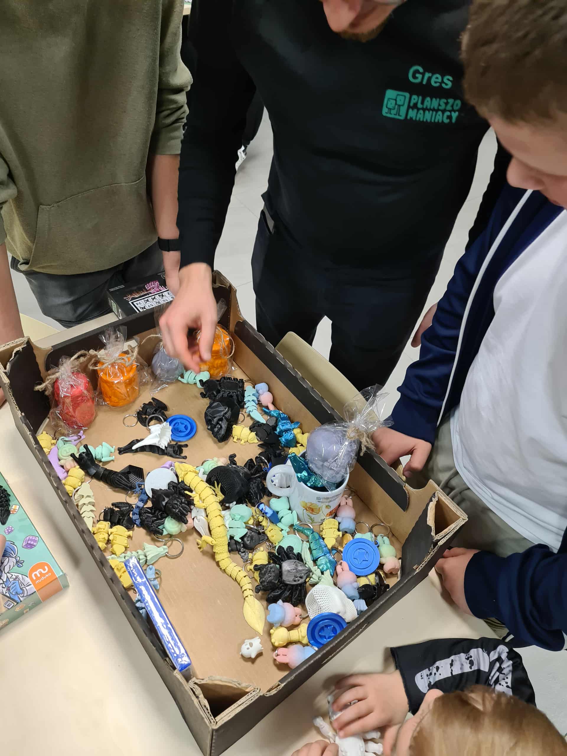 Uczestnicy wybierają figurki i gadżety z pudełka podczas spotkania z Planszomaniakami.
