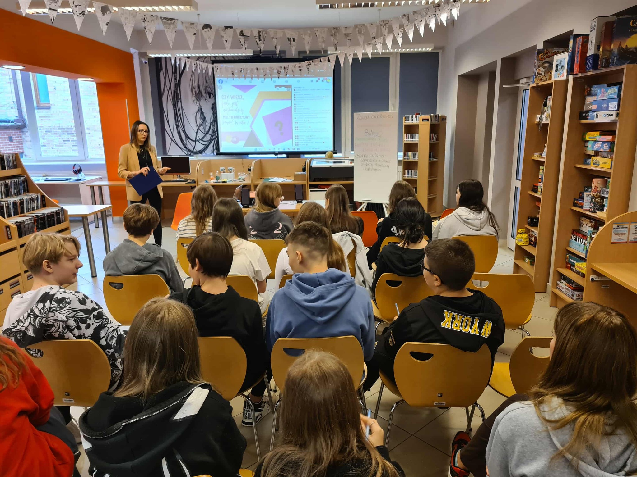 Prezentacja w bibliotece – prowadząca stoi przed grupą młodzieży, na ekranie wyświetlony quiz z pytaniem „Czy wiesz...?”.