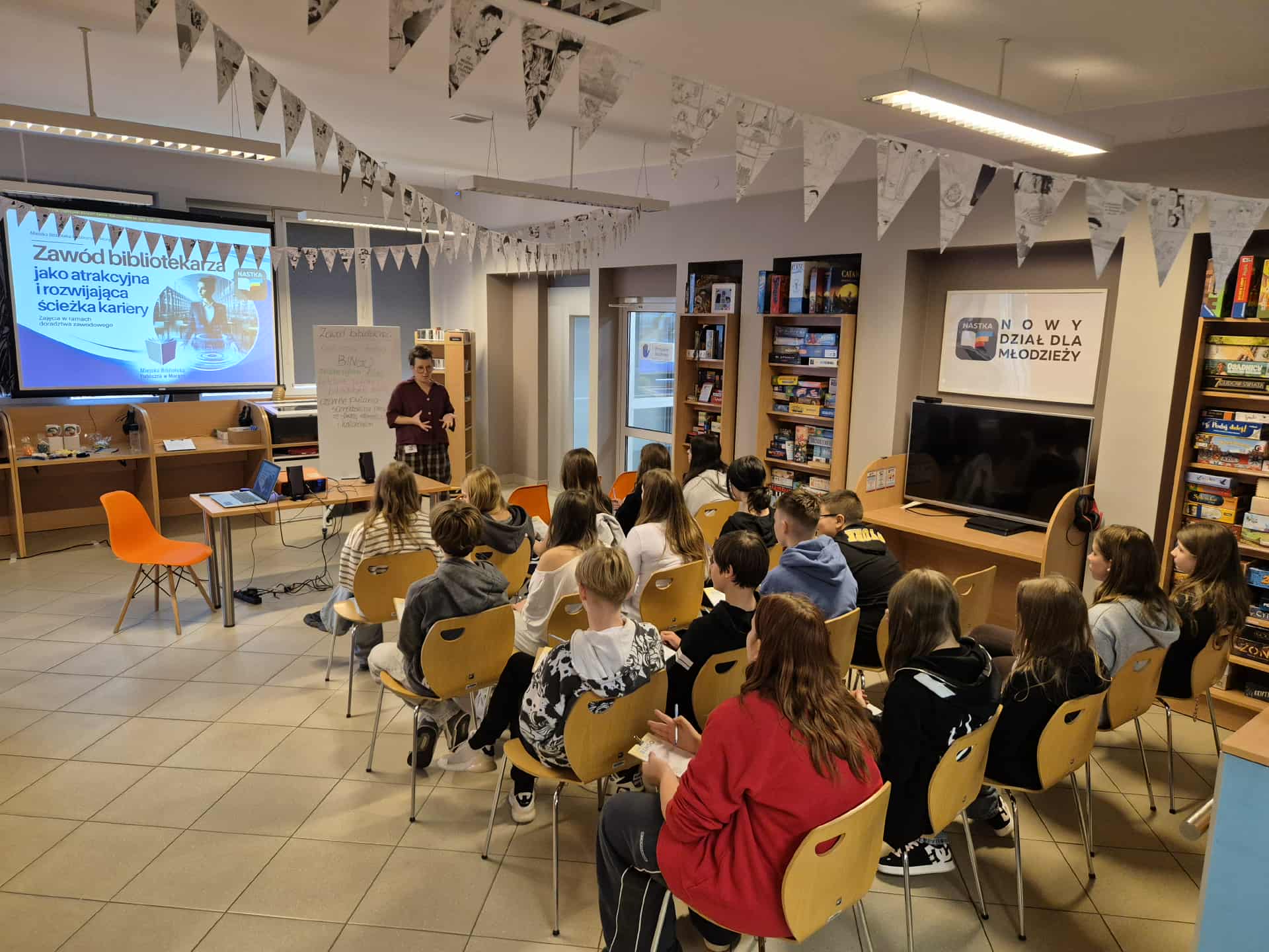 Spotkanie o zawodzie bibliotekarza, osoba prowadząca prezentuje slajd „Zawód bibliotekarza jako atrakcyjna i rozwijająca ścieżka kariery”.