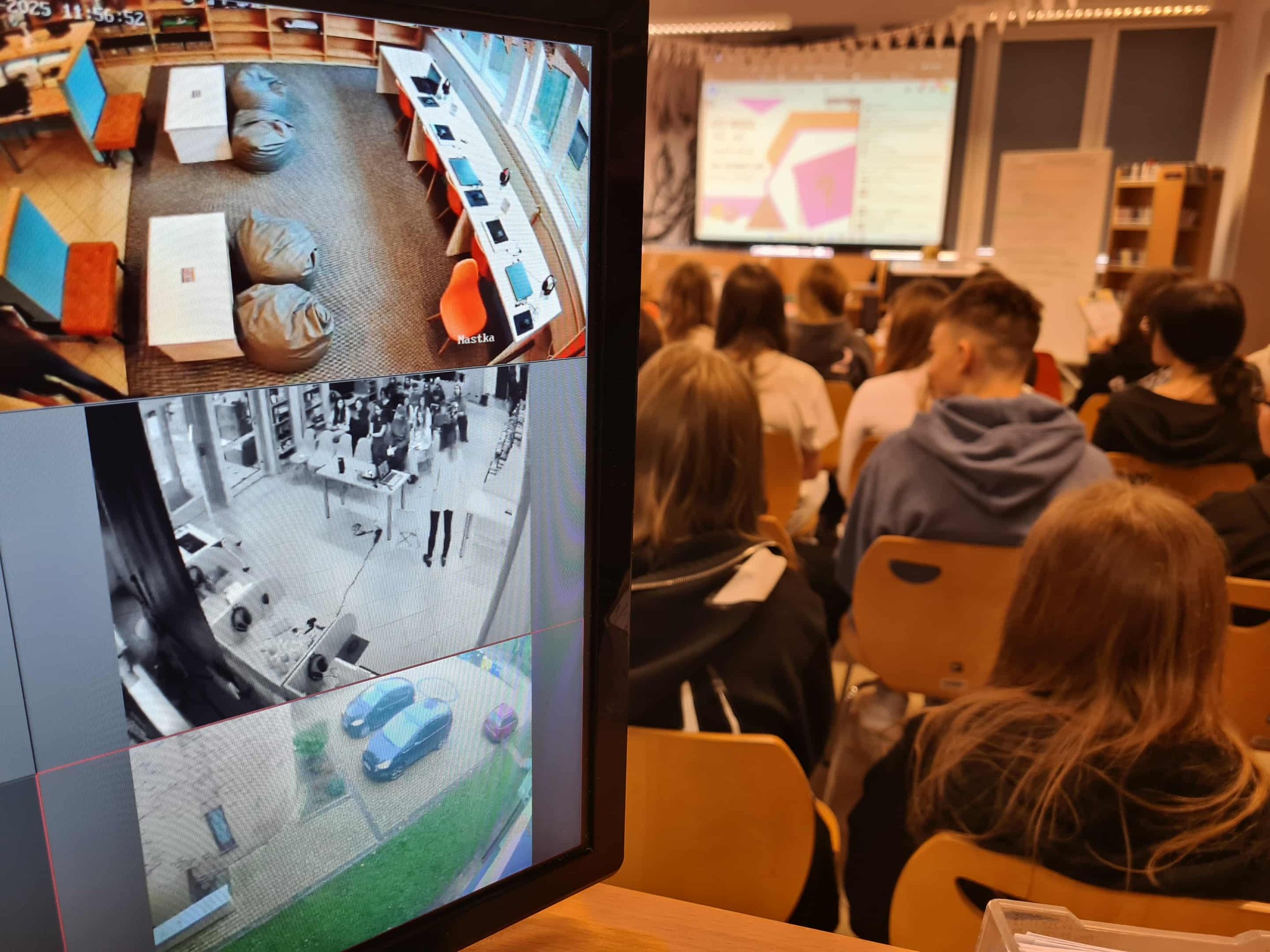 Widok sali z uczestnikami spotkania i monitorem pokazującym obraz z kamer, w tle trwa prezentacja.