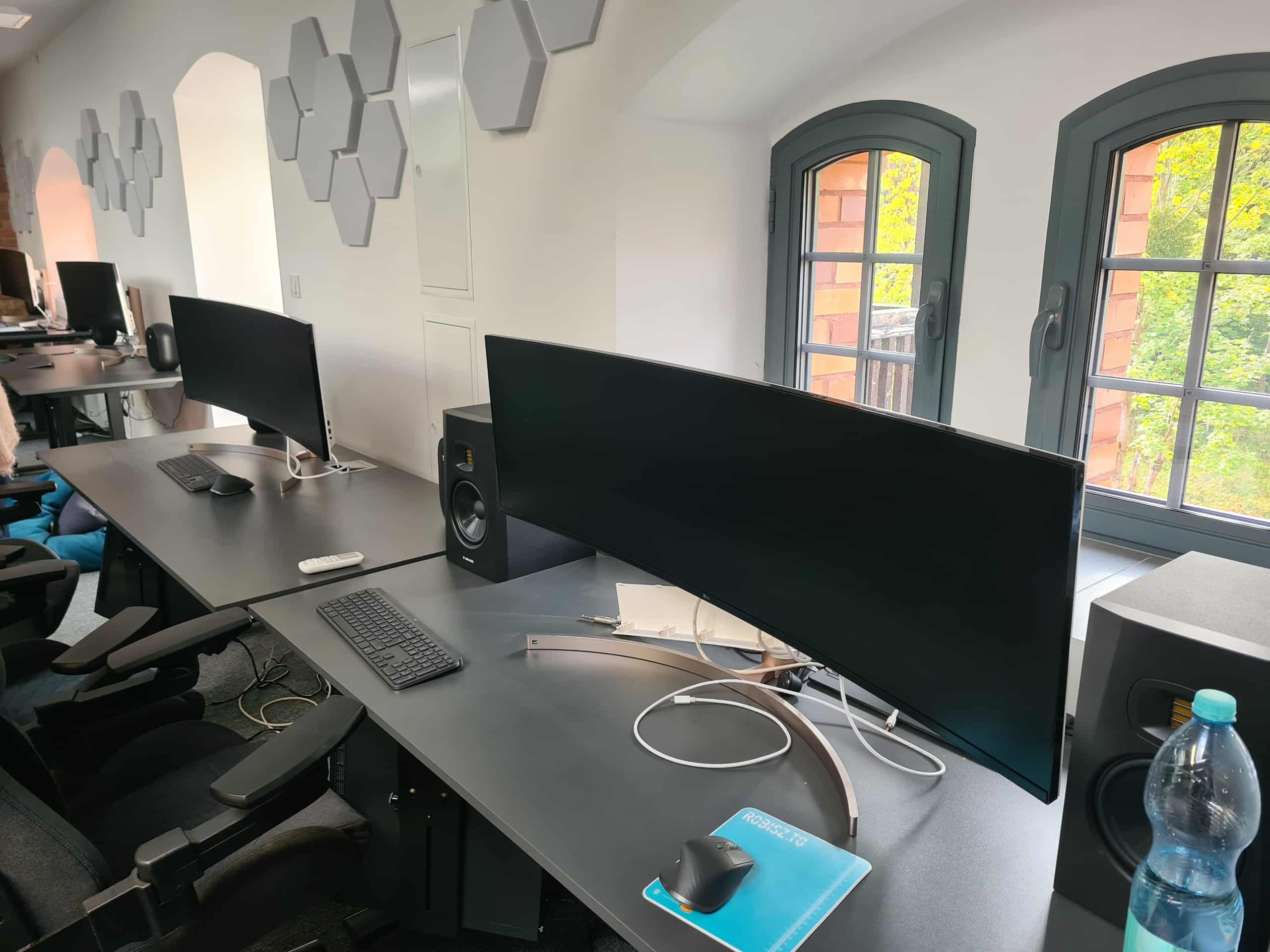 Stanowiska komputerowe z dużymi monitorami i sprzętem audio w nowoczesnej pracowni.