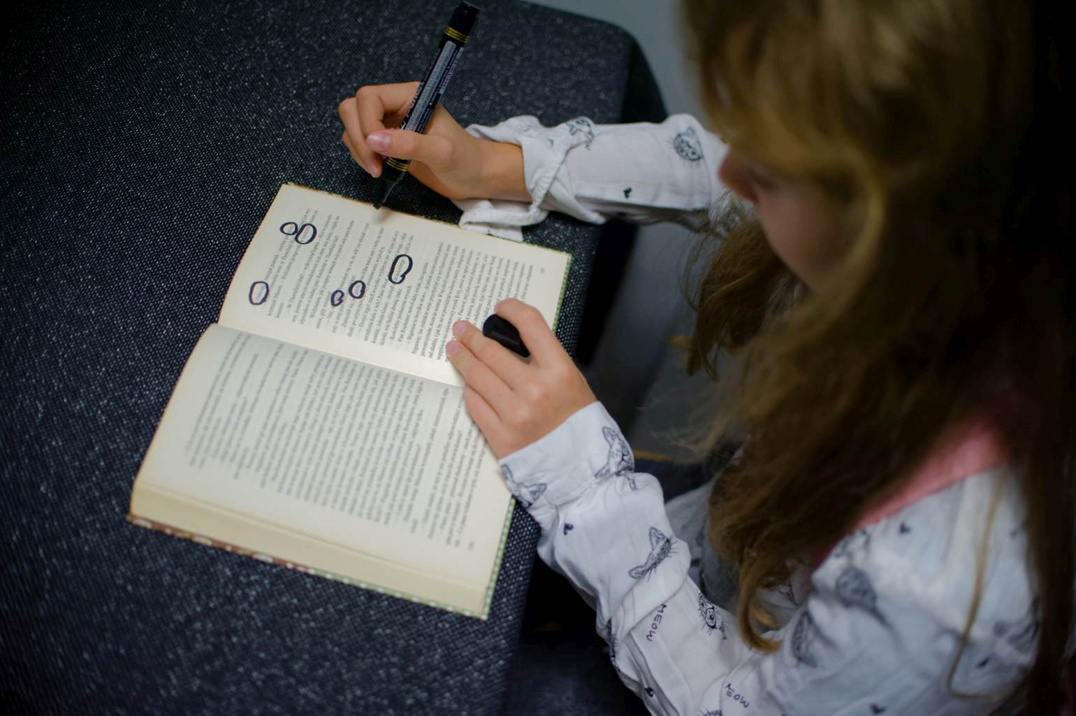 Osoba tworząca blackout poetry – siedzi przy stole i markerem zaznacza słowa w otwartej książce.