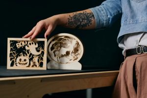 Drewniane dekoracje z motywami halloweenowymi wycięte laserowo, trzymane przez uczestniczkę warsztatów.