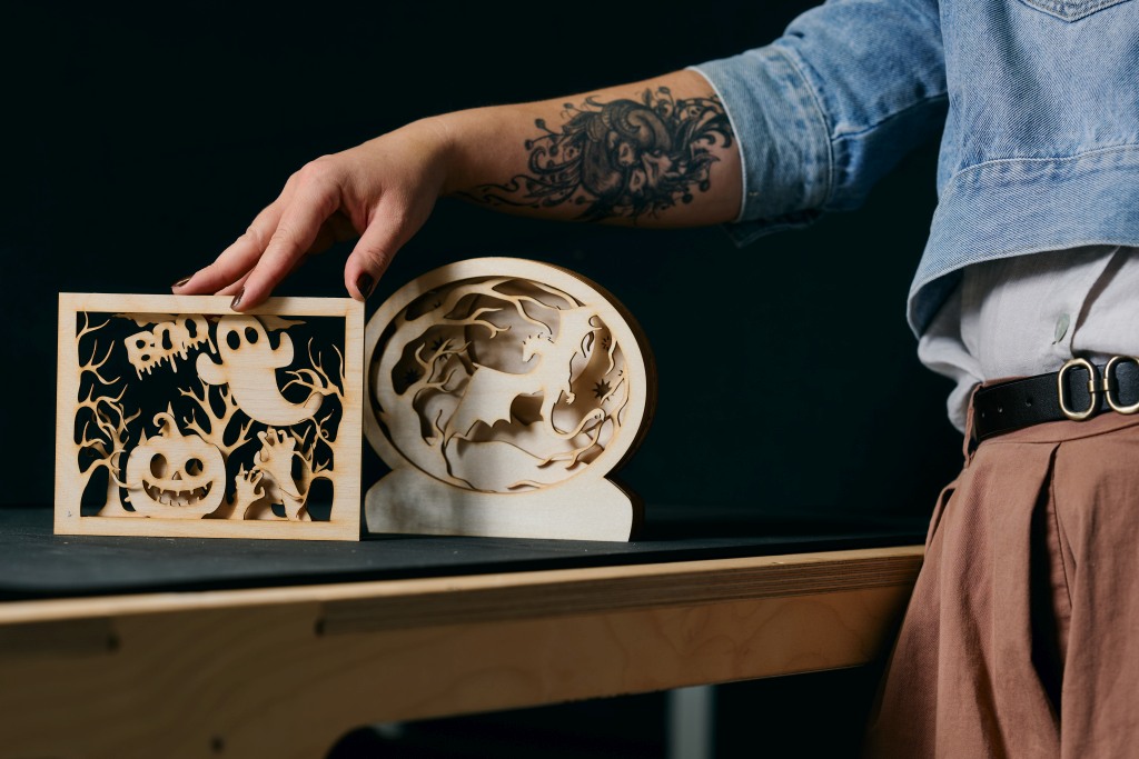 Drewniane dekoracje z motywami halloweenowymi wycięte laserowo, trzymane przez uczestniczkę warsztatów.