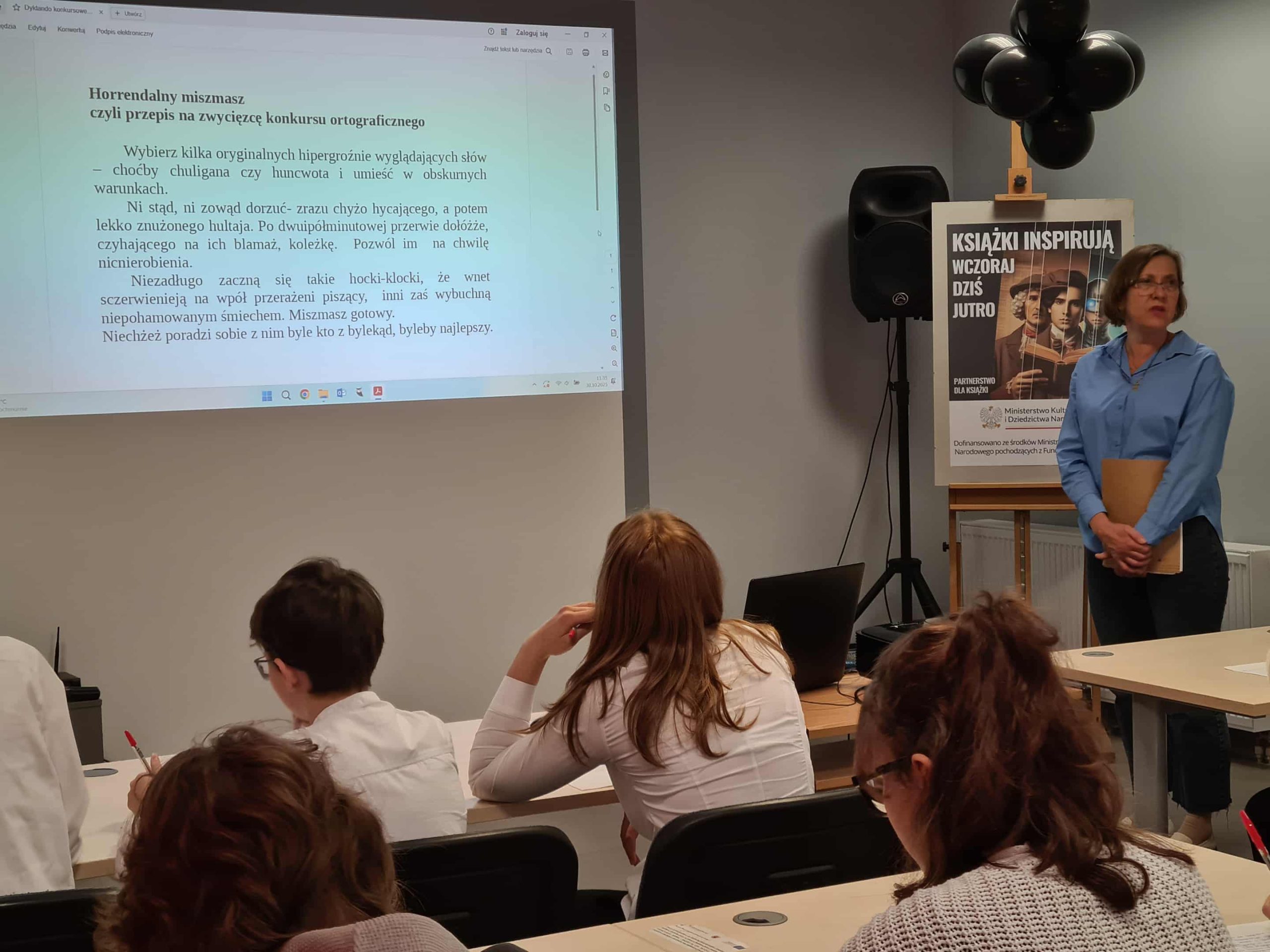 Prowadząca konkurs przedstawia zasady ortograficzne uczestnikom w sali biblioteki.