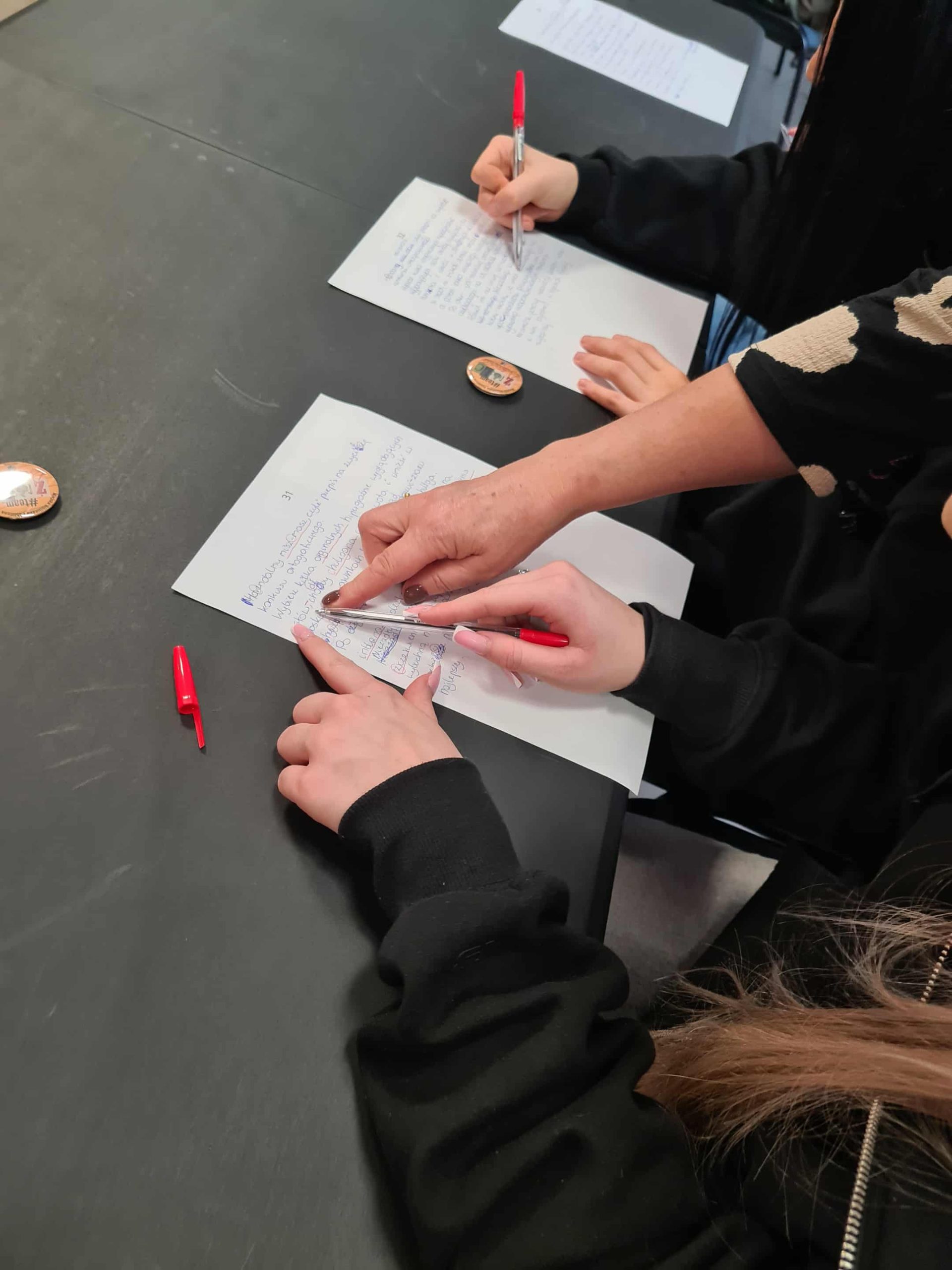 Uczestnicy piszą dyktando, nauczycielka poprawia tekst z jedną z osób.