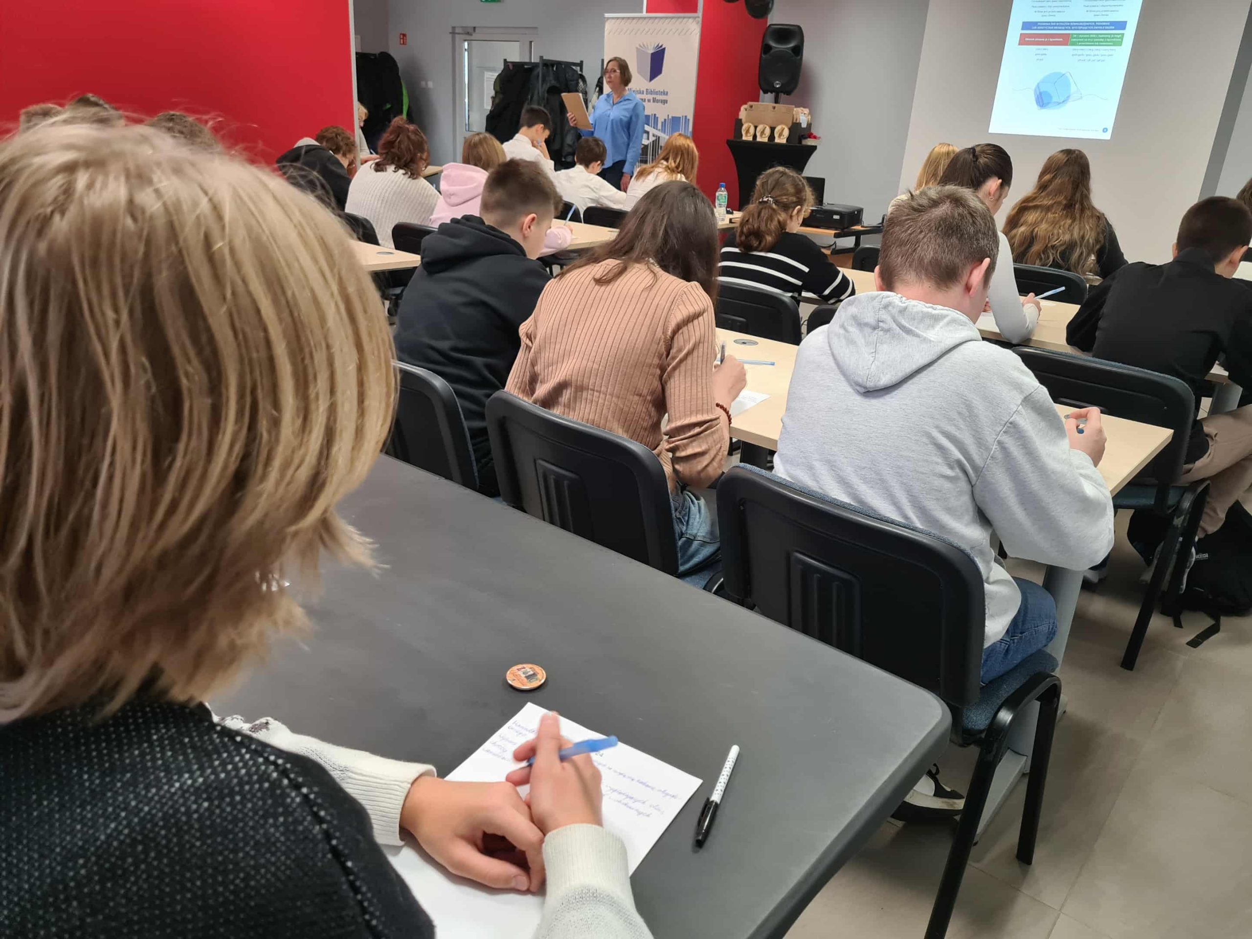 Uczestnicy pochylają się nad kartkami, pisząc tekst dyktanda.