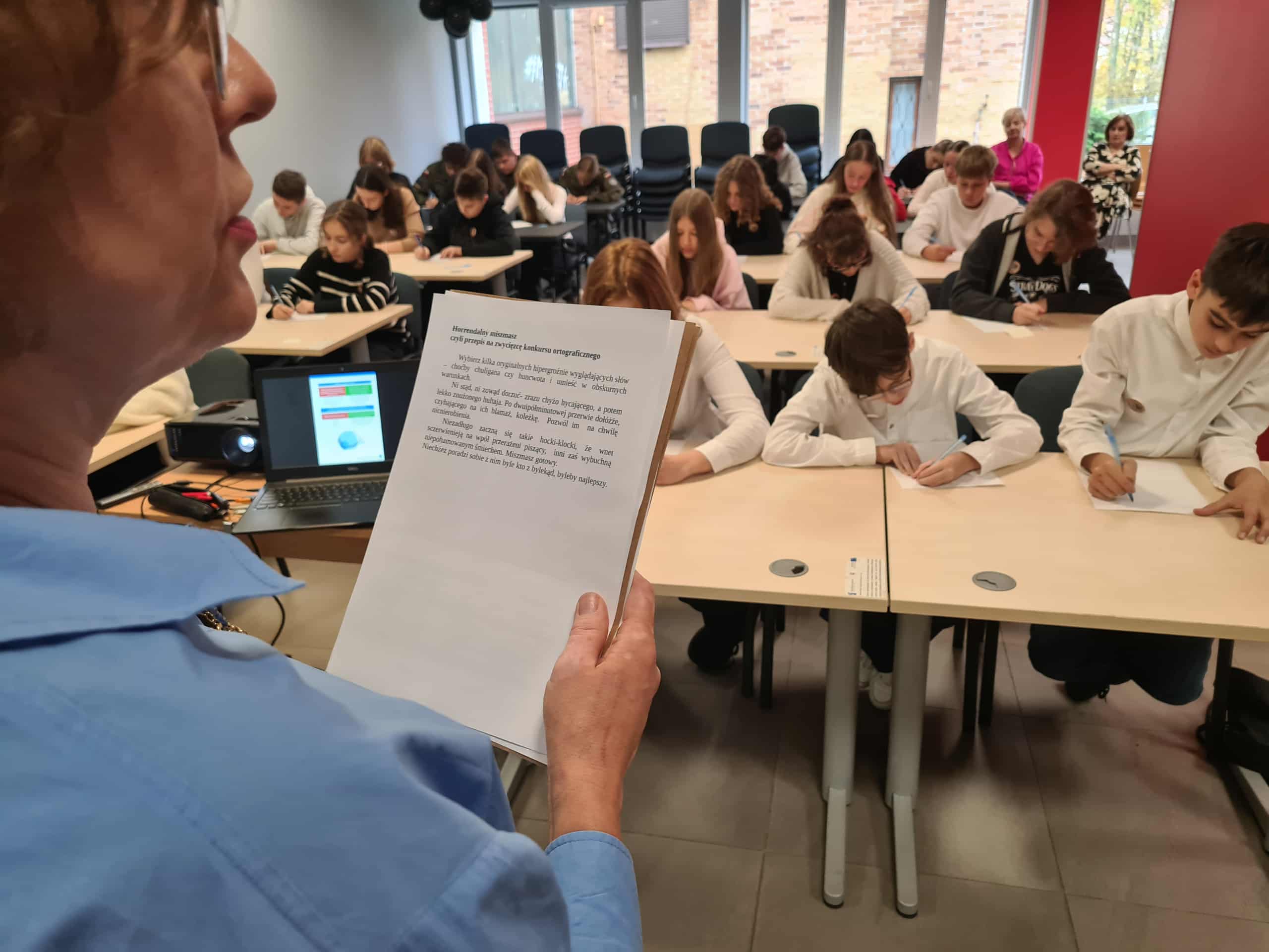 Prowadząca czyta tekst dyktanda, a uczestnicy zapisują słowa na kartkach.