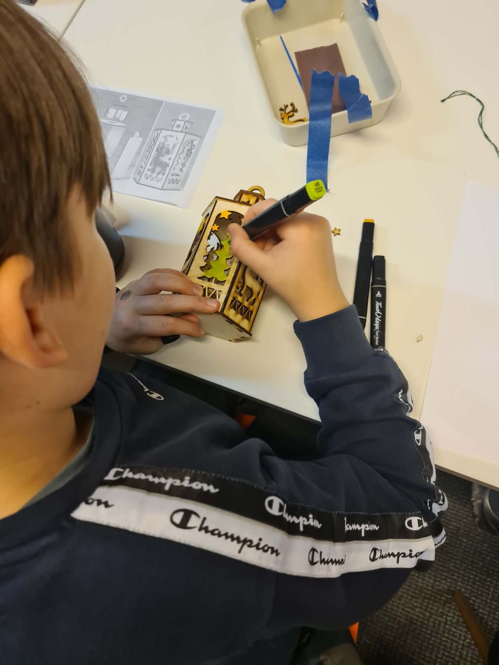 Zbliżenie na ręce dziecka dekorującego drewniany lampion markerem.