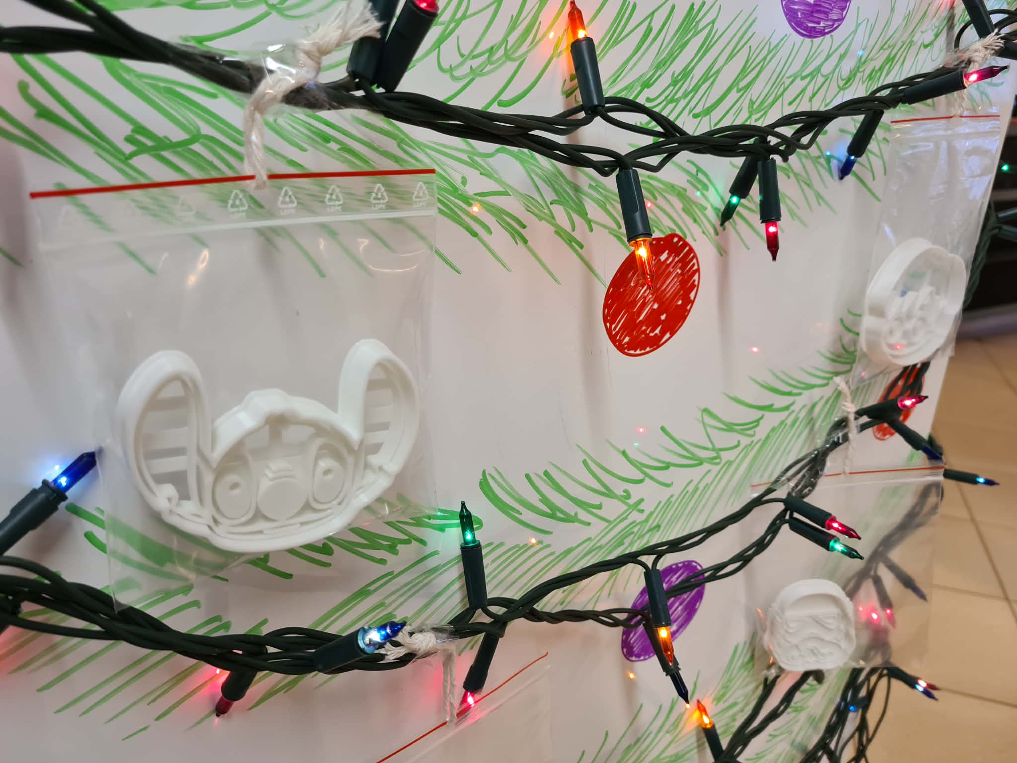 Zbliżenie na foremkę 3D w kształcie Sticha, zawieszoną na tablicy ze światełkami.