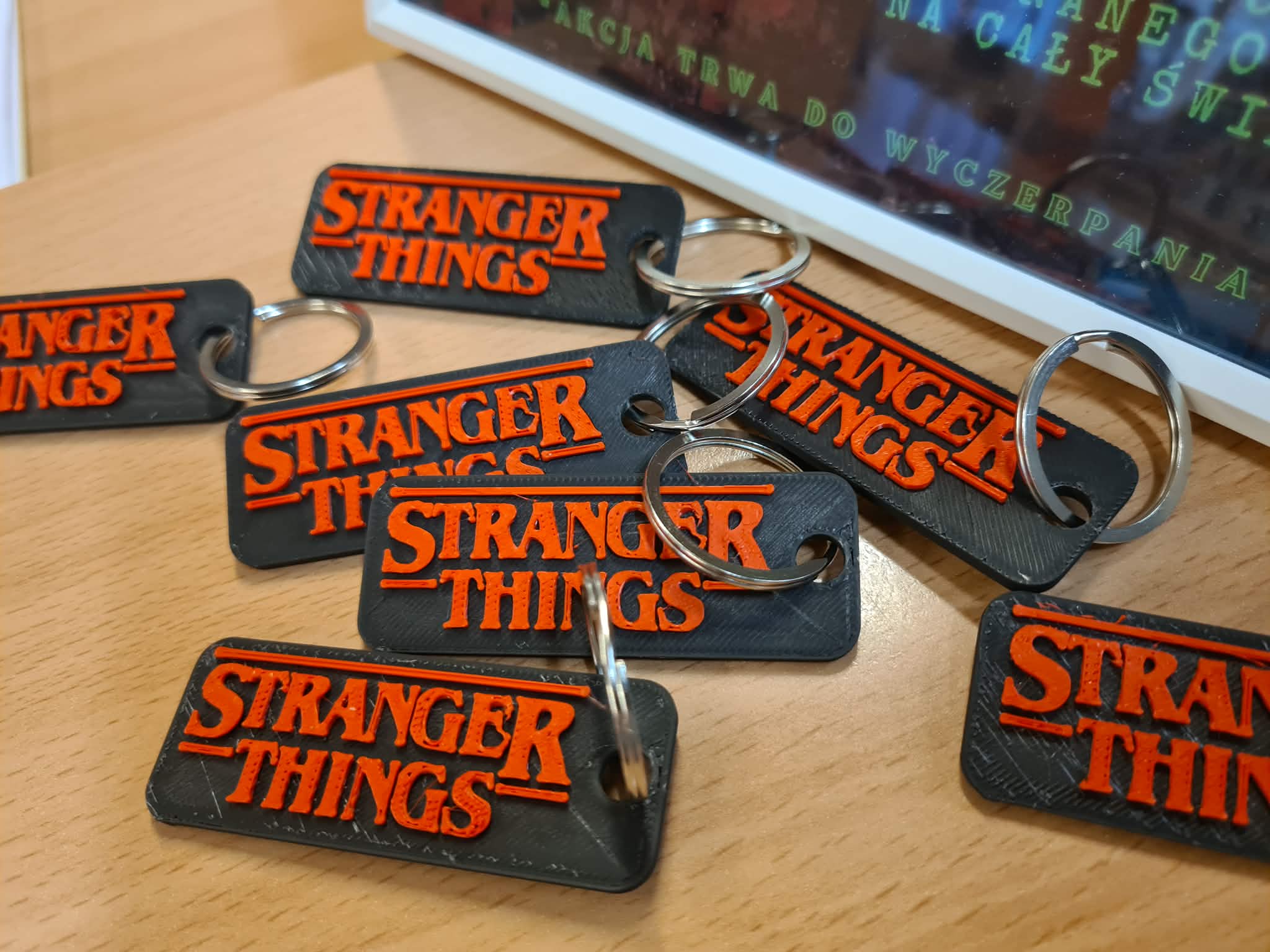 „Kilka czarnych breloczków z czerwonym napisem Stranger Things leży na drewnianym blacie.