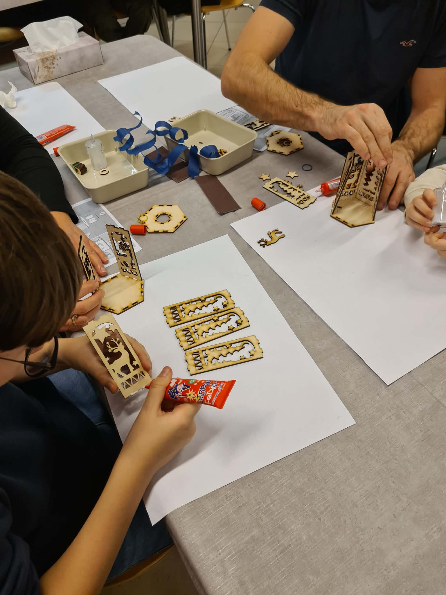 Dorośli i dzieci wspólnie montują lampion przy stole.