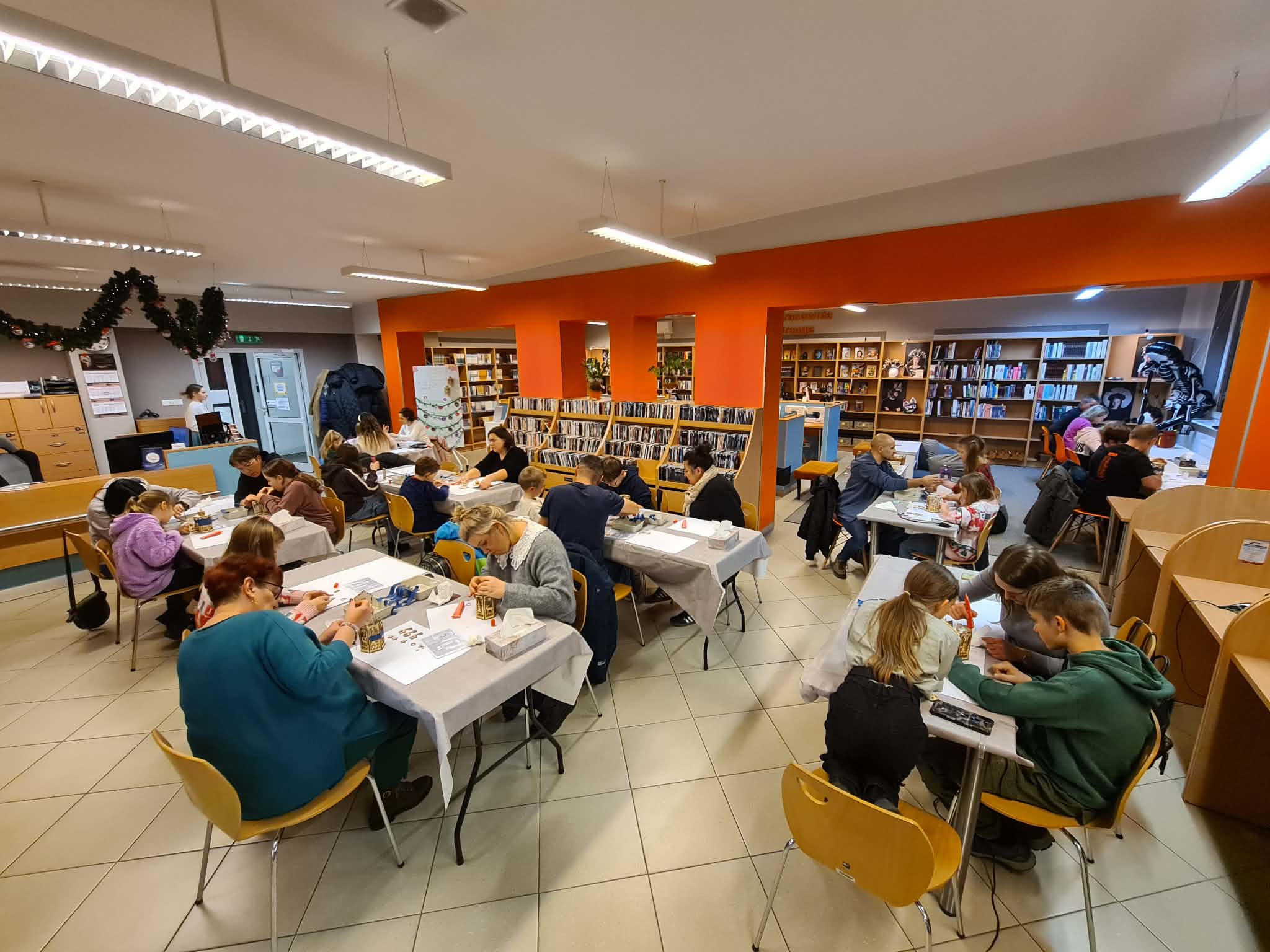 Widok sali biblioteki wypełnionej uczestnikami rodzinnych warsztatów.