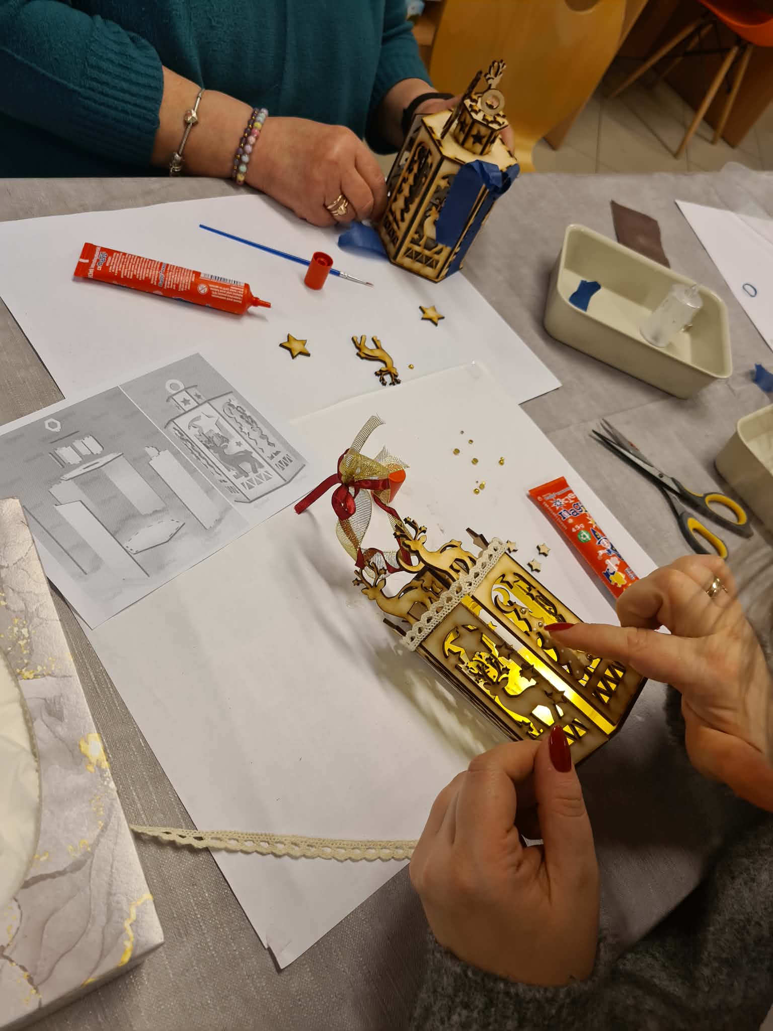 Dorośli i dzieci wspólnie montują lampion przy stole.