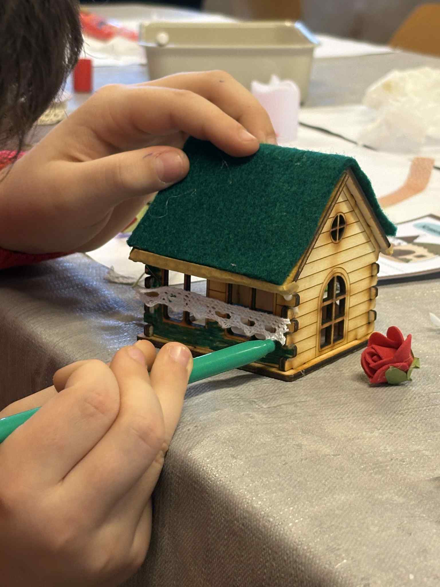 Dziecko koloruje element drewnianego domku zielonym pisakiem, domek ma filcowy dach.