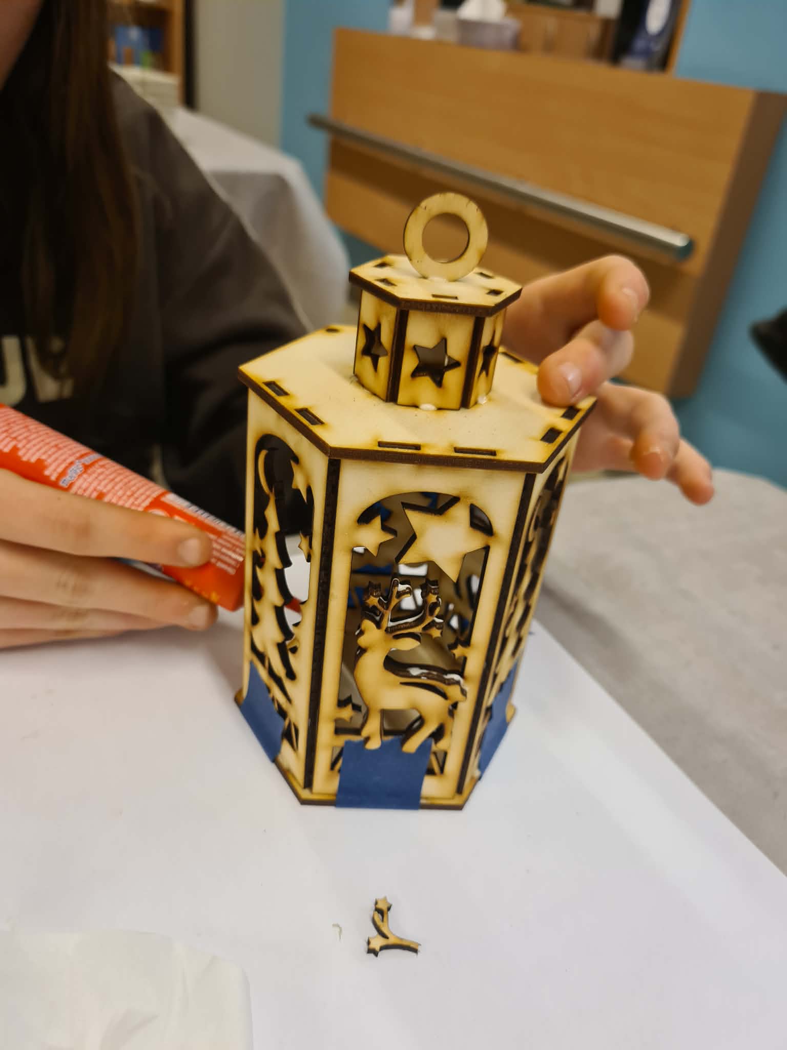 Dziecko skleja drewnianą latarenkę na stole.