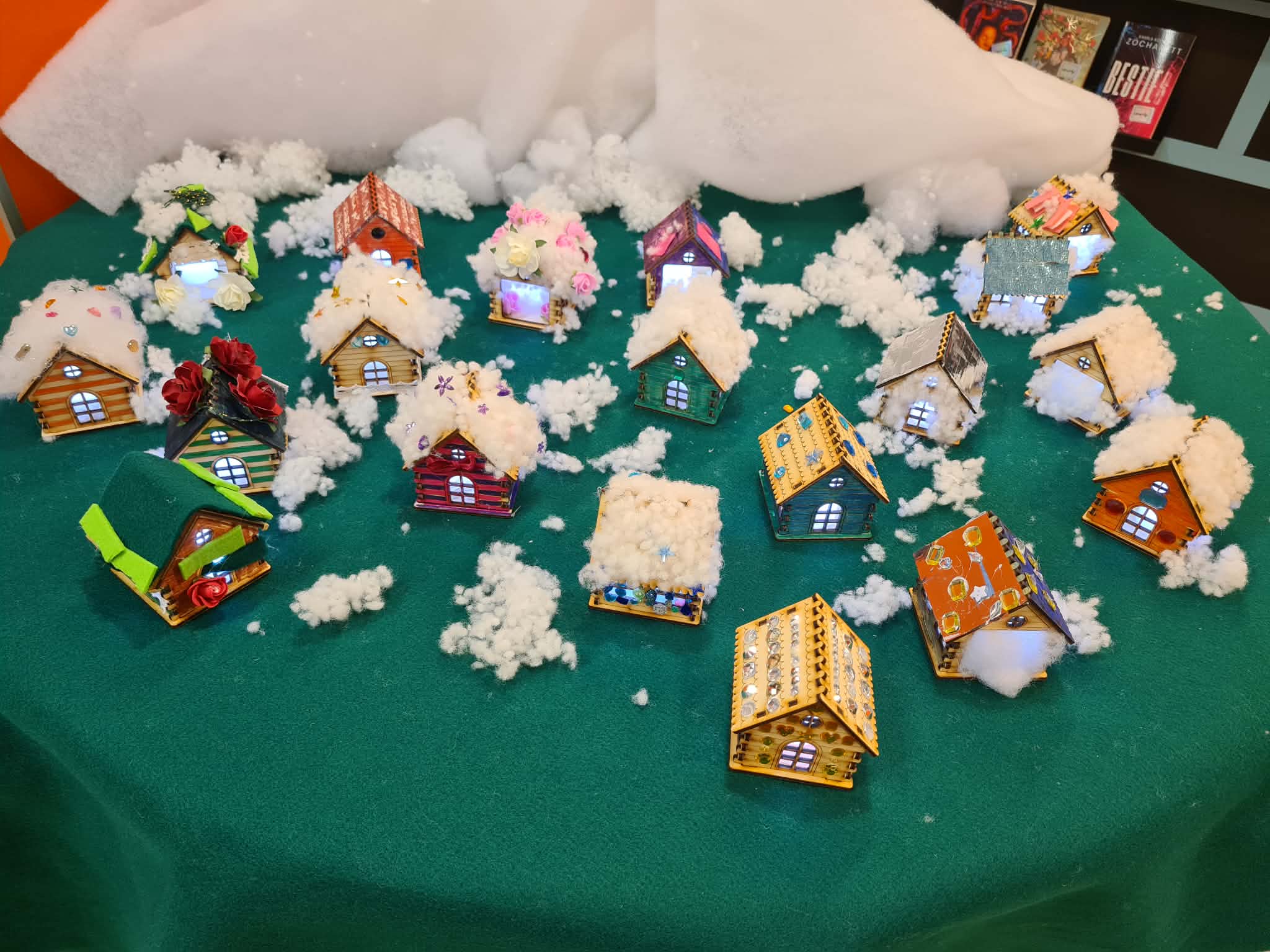 Dziesiątki kolorowych, świecących domków ustawionych na zielonym materiale, otoczonych sztucznym śniegiem.