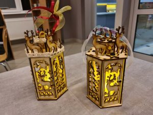 Dwie złożone ozdobione kokardkami i świecące drewniane latarenki stoją na stole.