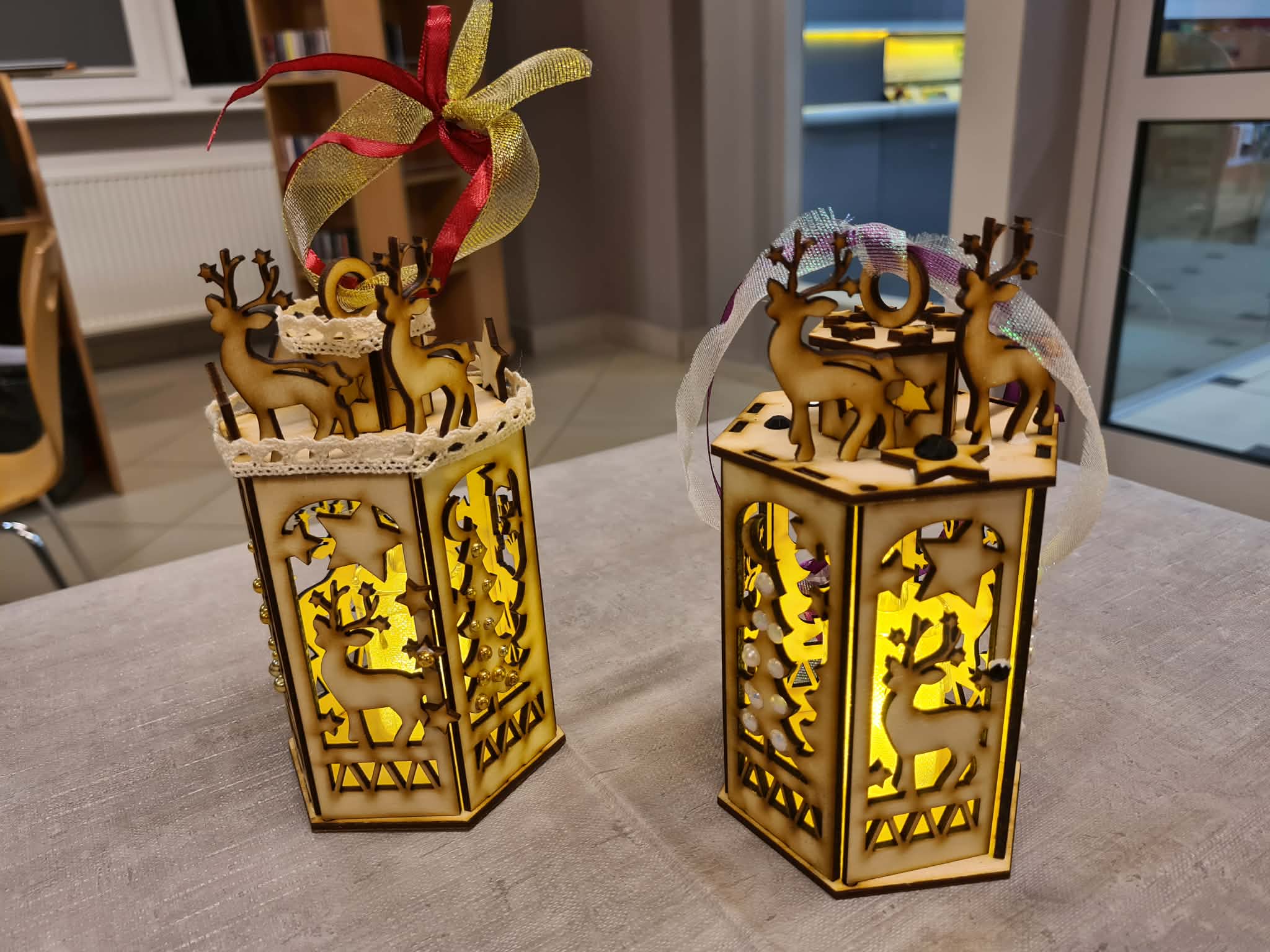 Dwie złożone ozdobione kokardkami i świecące drewniane latarenki stoją na stole.