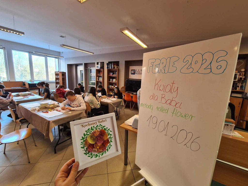 Sala warsztatowa z dziećmi pracującymi przy stołach; na tablicy napis „Ferie 2026 – Kwiaty dla Babci”.