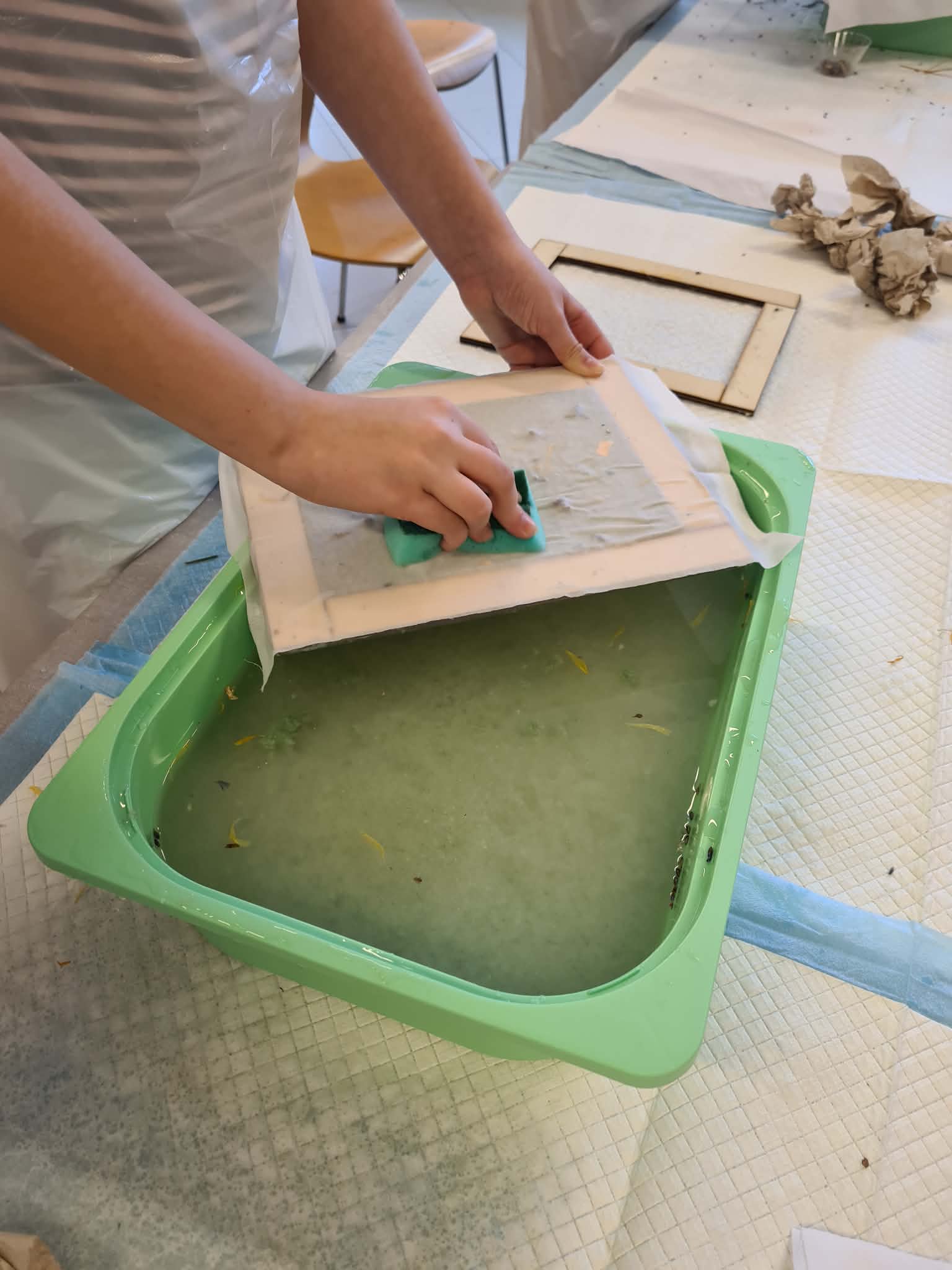 Osoba odsącza wodę z papieru czerpanego gąbką nad miską.