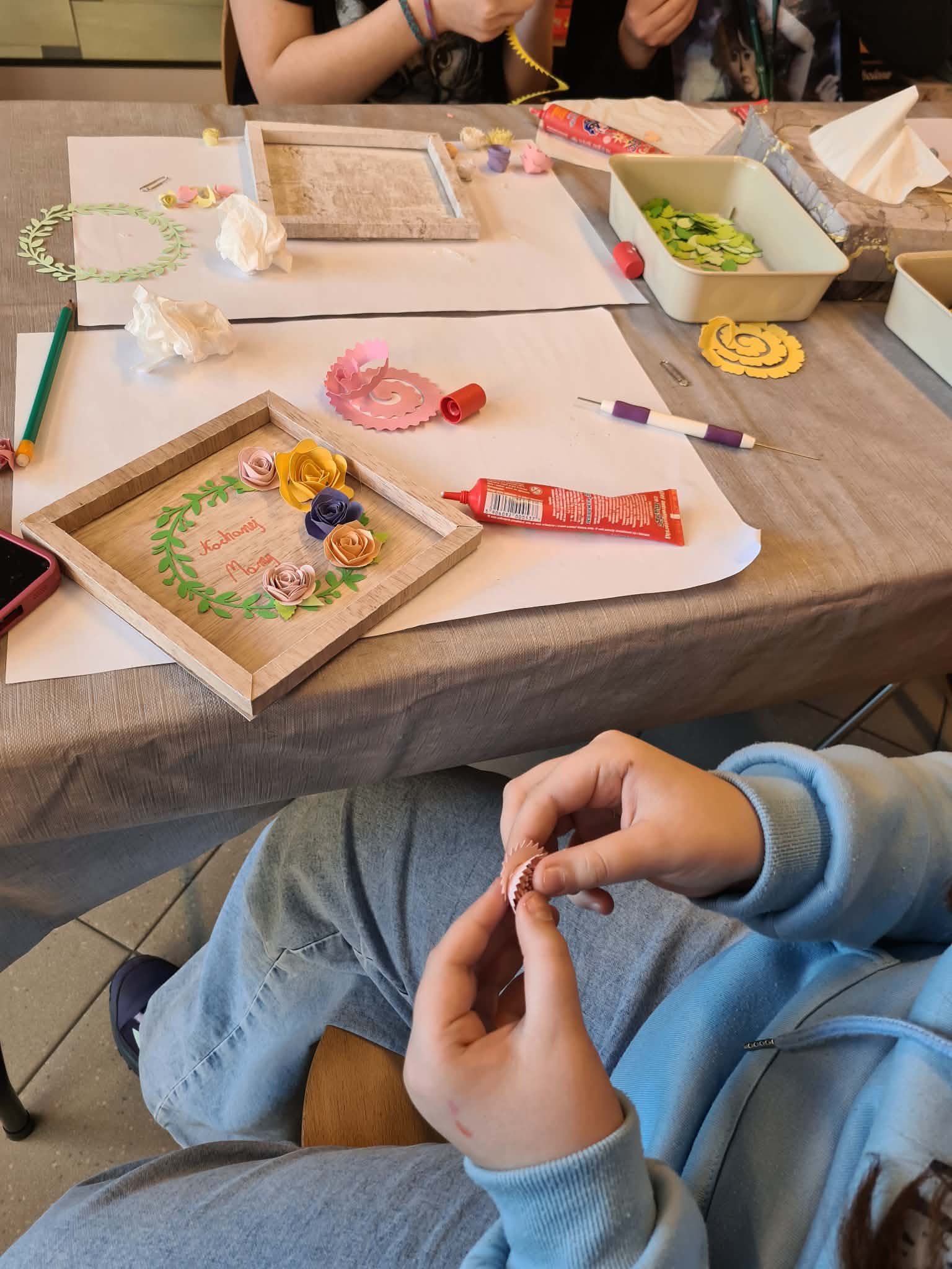 Uczestnik zwija papierowy element kwiatu podczas pracy plastycznej.