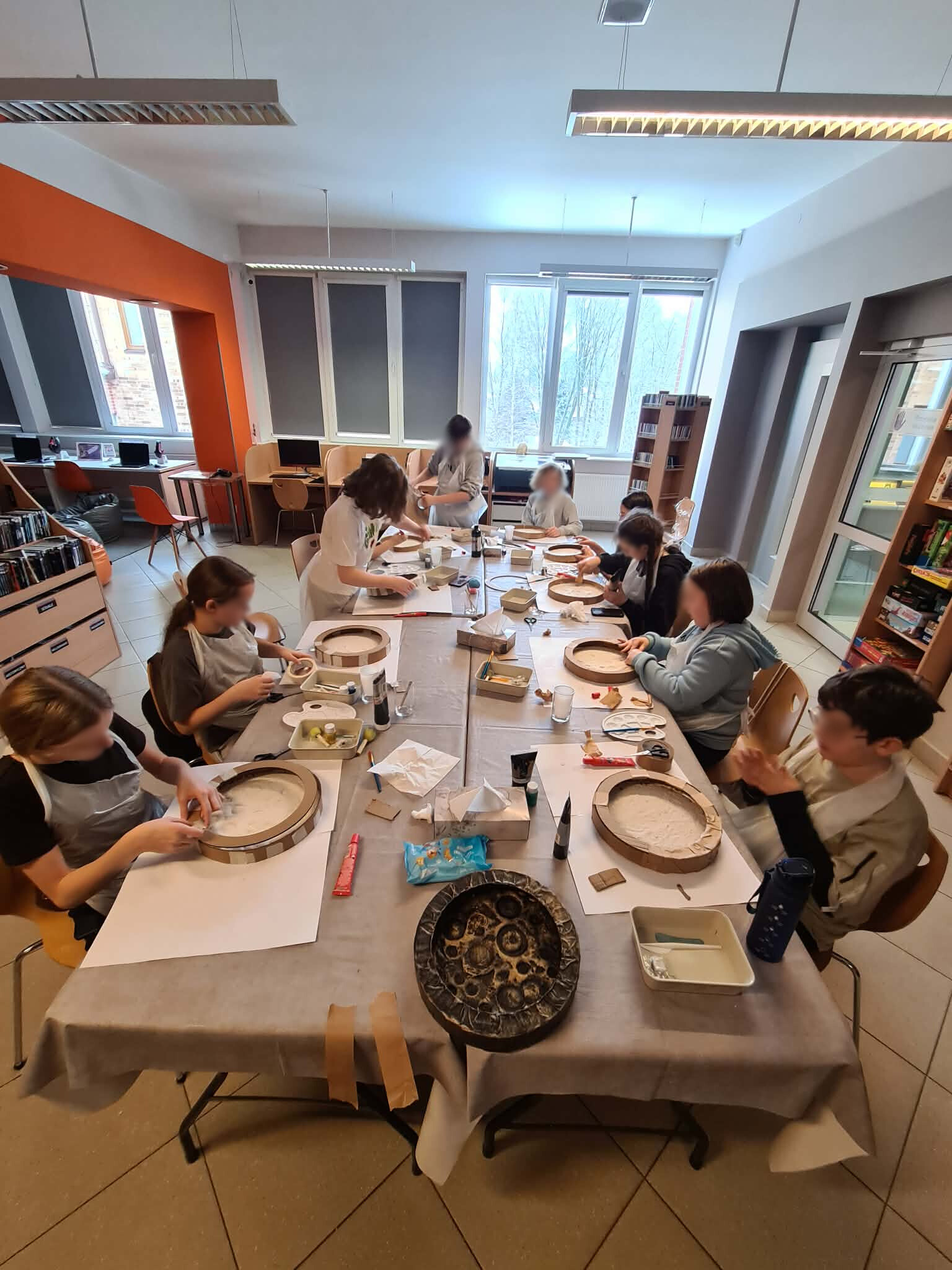 Uczestnicy warsztatów pracują przy długim stole w bibliotece.