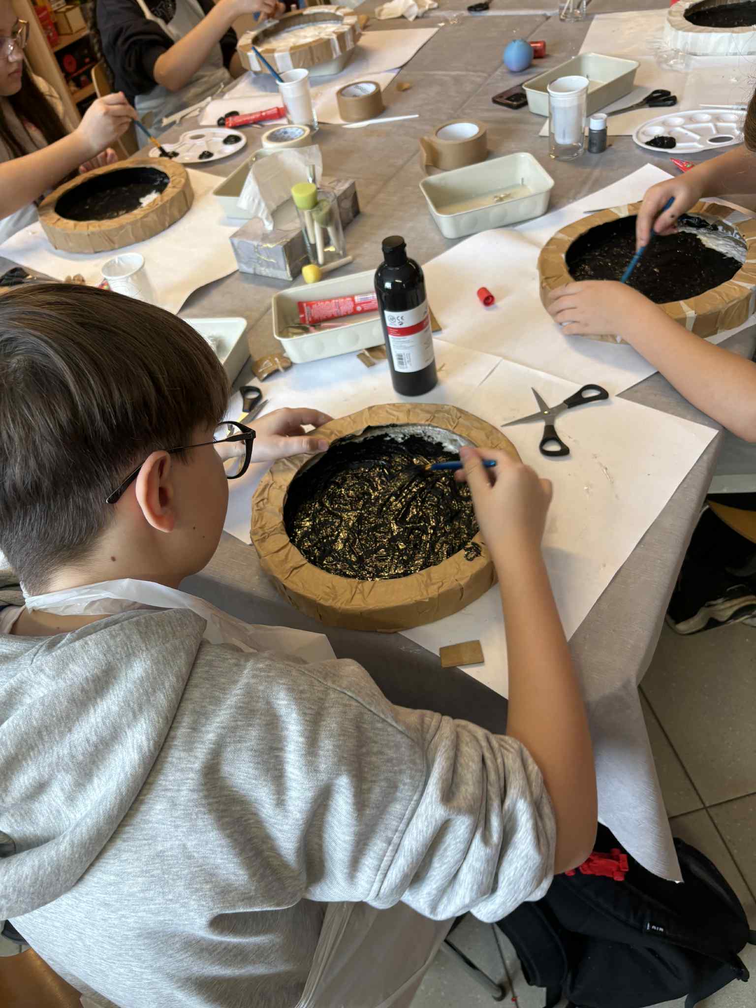 Dzieci malują wnętrza okrągłych form czarną i złotą farbą.
