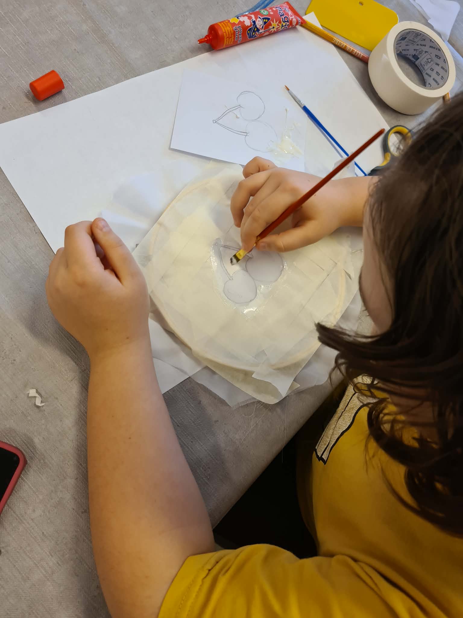 Dziecko maluje wzór na tkaninie rozpiętej w tamborku.