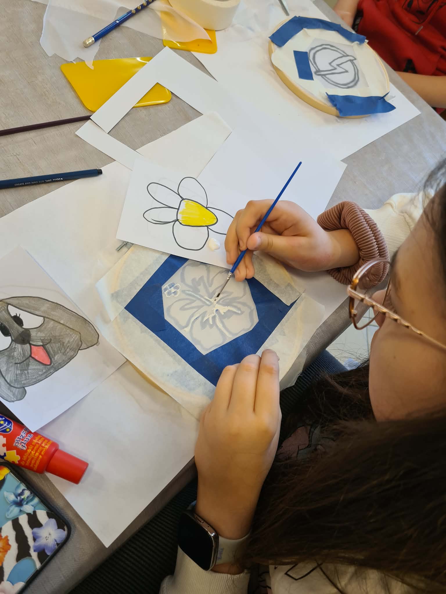 Dziecko precyzyjnie maluje wzór farbą na materiale zabezpieczonym taśmą.