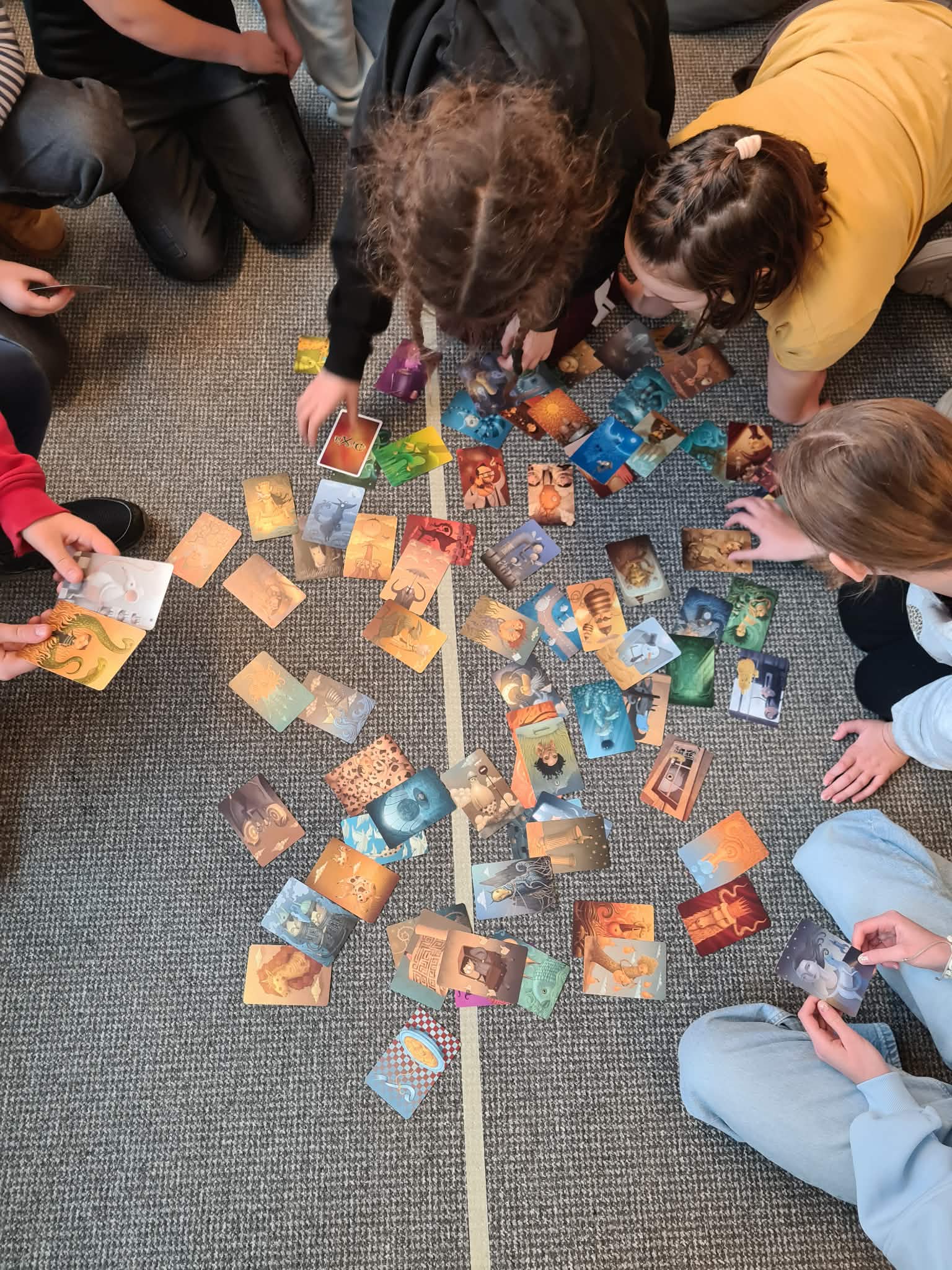 Grupa dzieci na podłodze układa i ogląda ilustrowane karty.