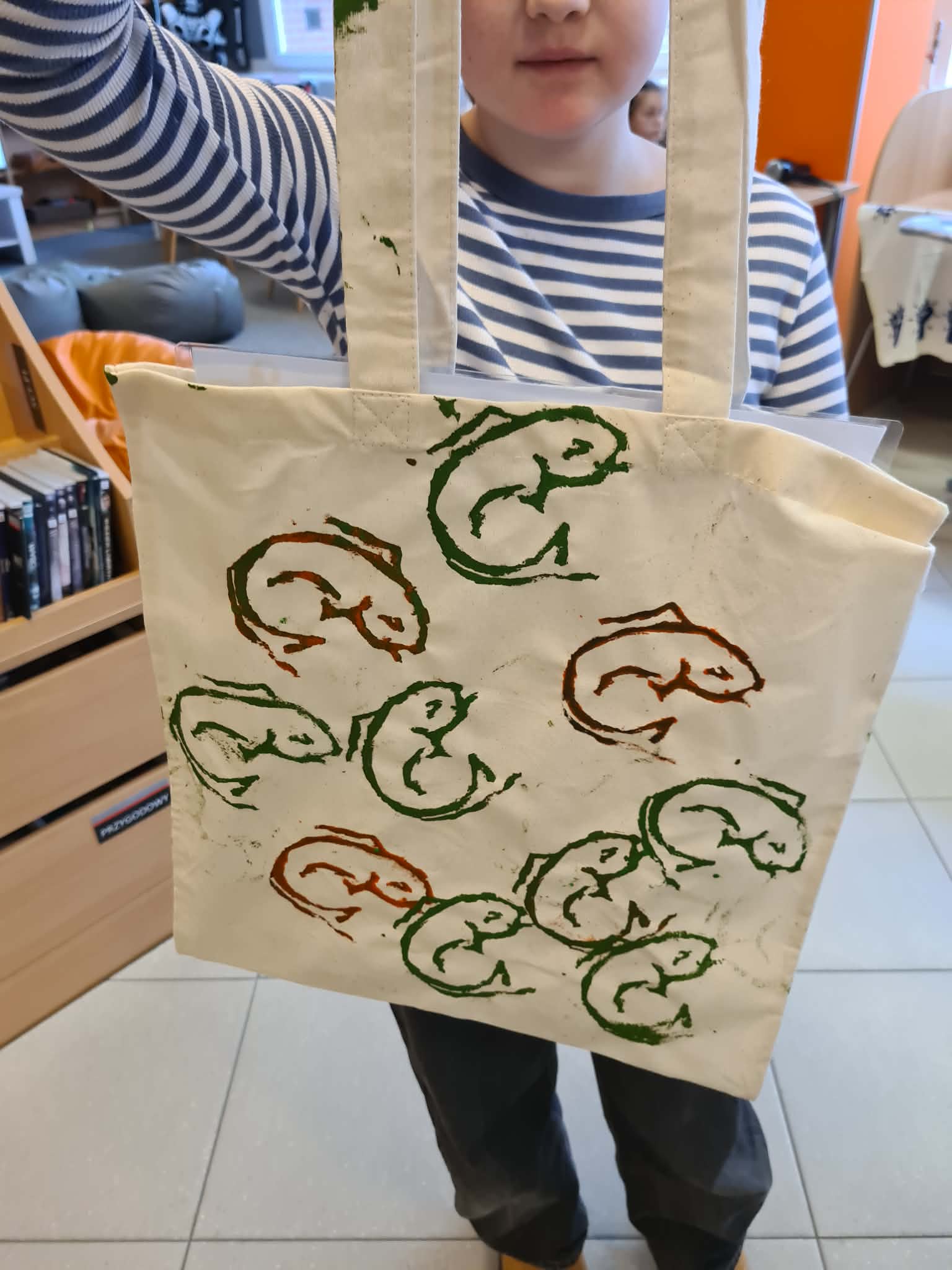 Dziecko prezentuje bawełnianą torbę z ręcznie wykonanym nadrukiem.