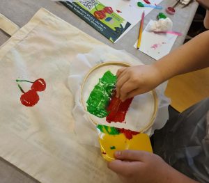 Dziecko maluje farbami wzór na tkaninie rozpiętej w tamborku.