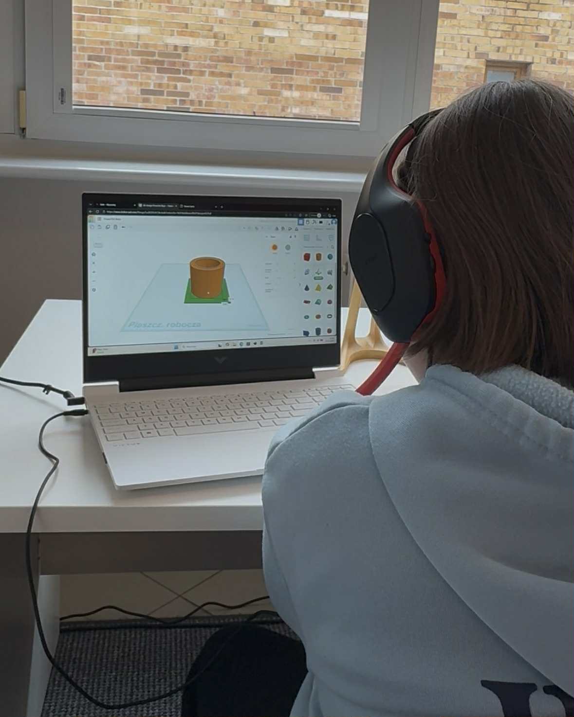 Uczestniczka projektuje model 3D na laptopie w słuchawkach.