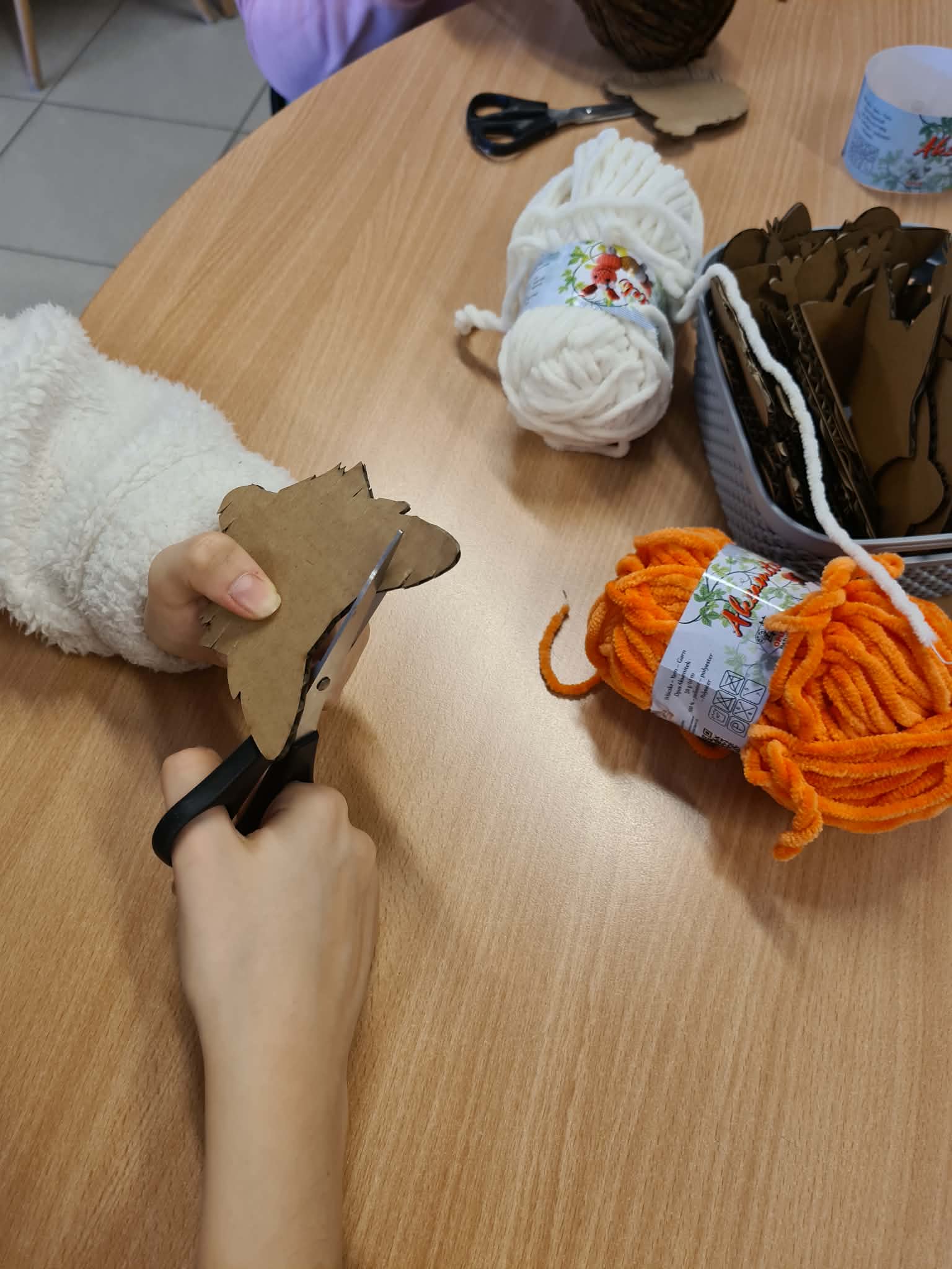 Dłonie dziecka wycinające kartonowy kształt nożyczkami.