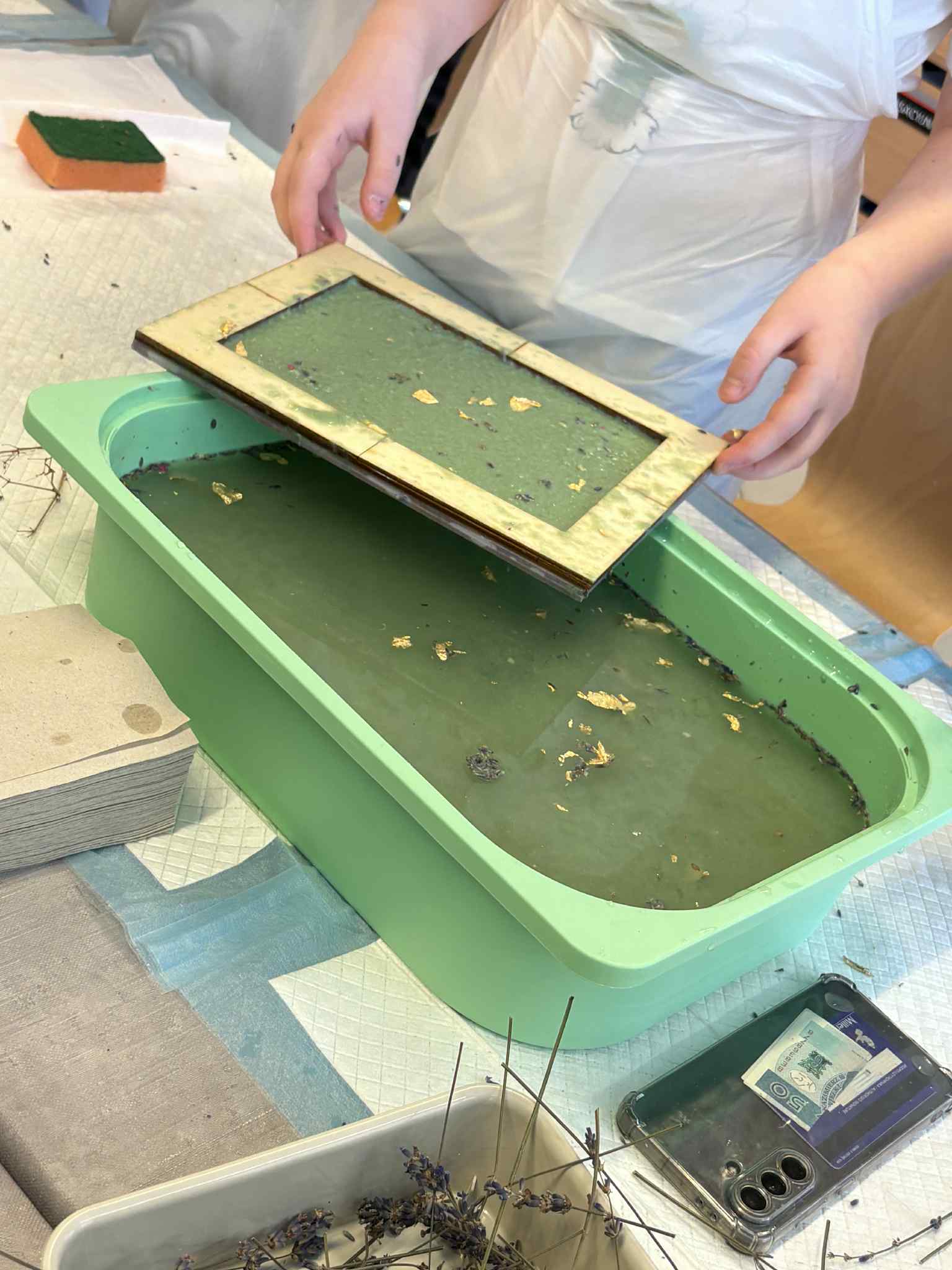 Rama do papieru czerpanego zanurzana w zielonej misce z masą papierową.