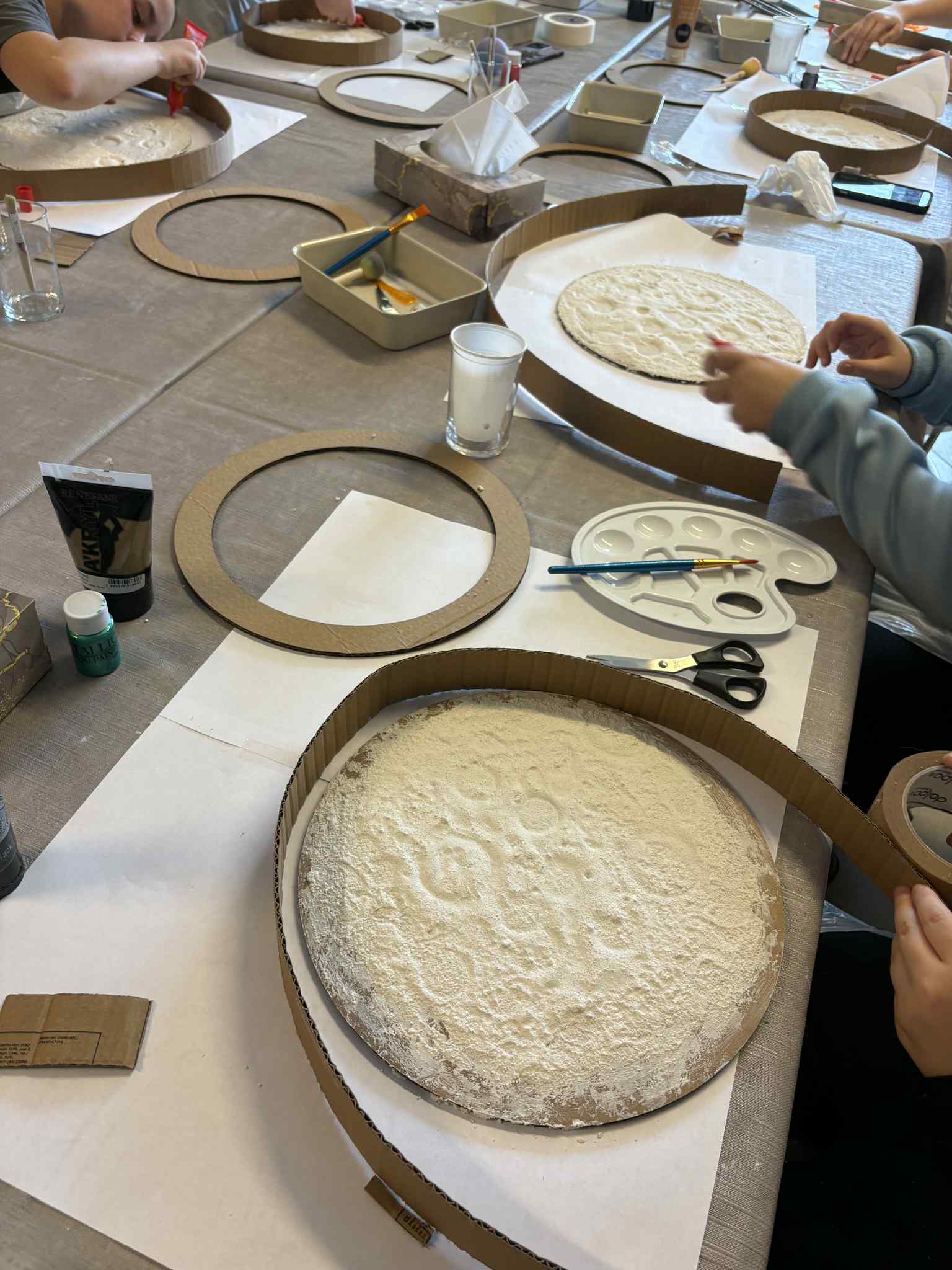 Kilka stanowisk pracy z okrągłymi formami i materiałami plastycznymi.