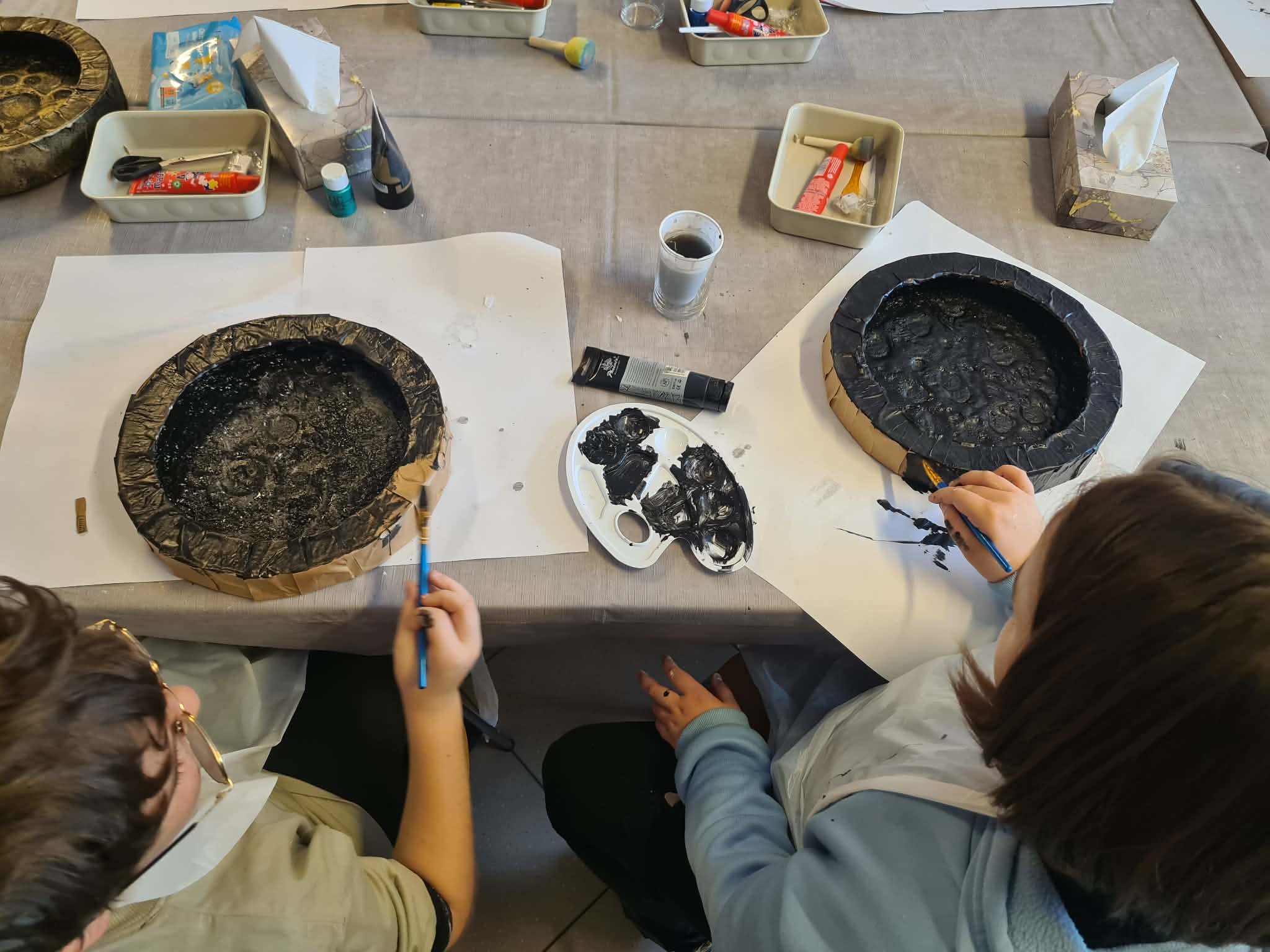 Uczestnicy malują okrągłe formy czarną farbą.