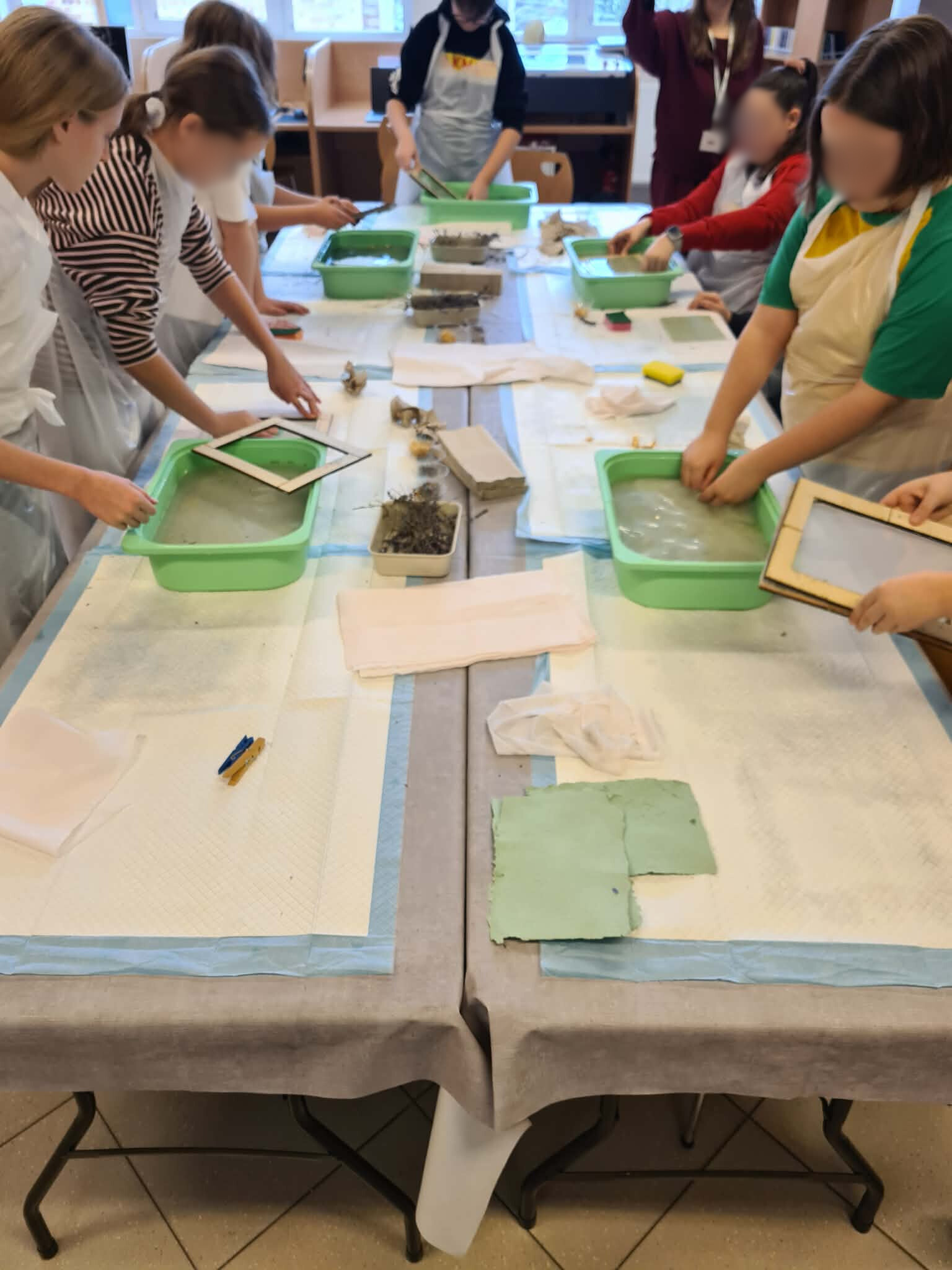 Dzieci pracują przy stołach, czerpiąc papier w zielonych miskach.