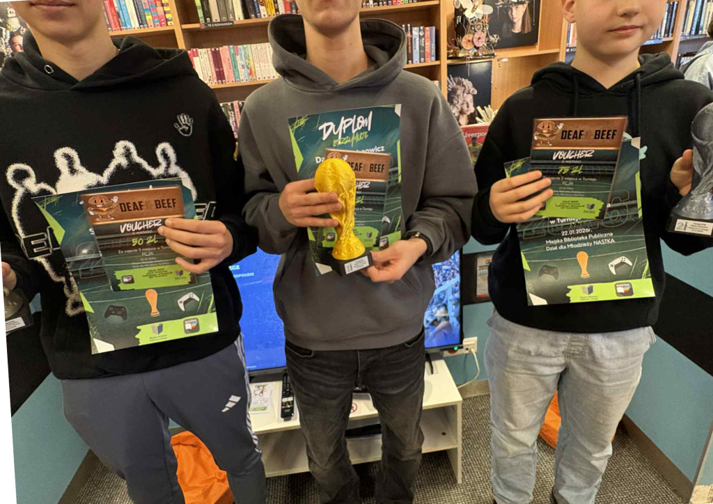 Trzech nastolatków trzyma dyplomy i nagrody po turnieju gier. Jeden z nich trzyma złoty puchar w kształcie trofeum piłkarskiego.