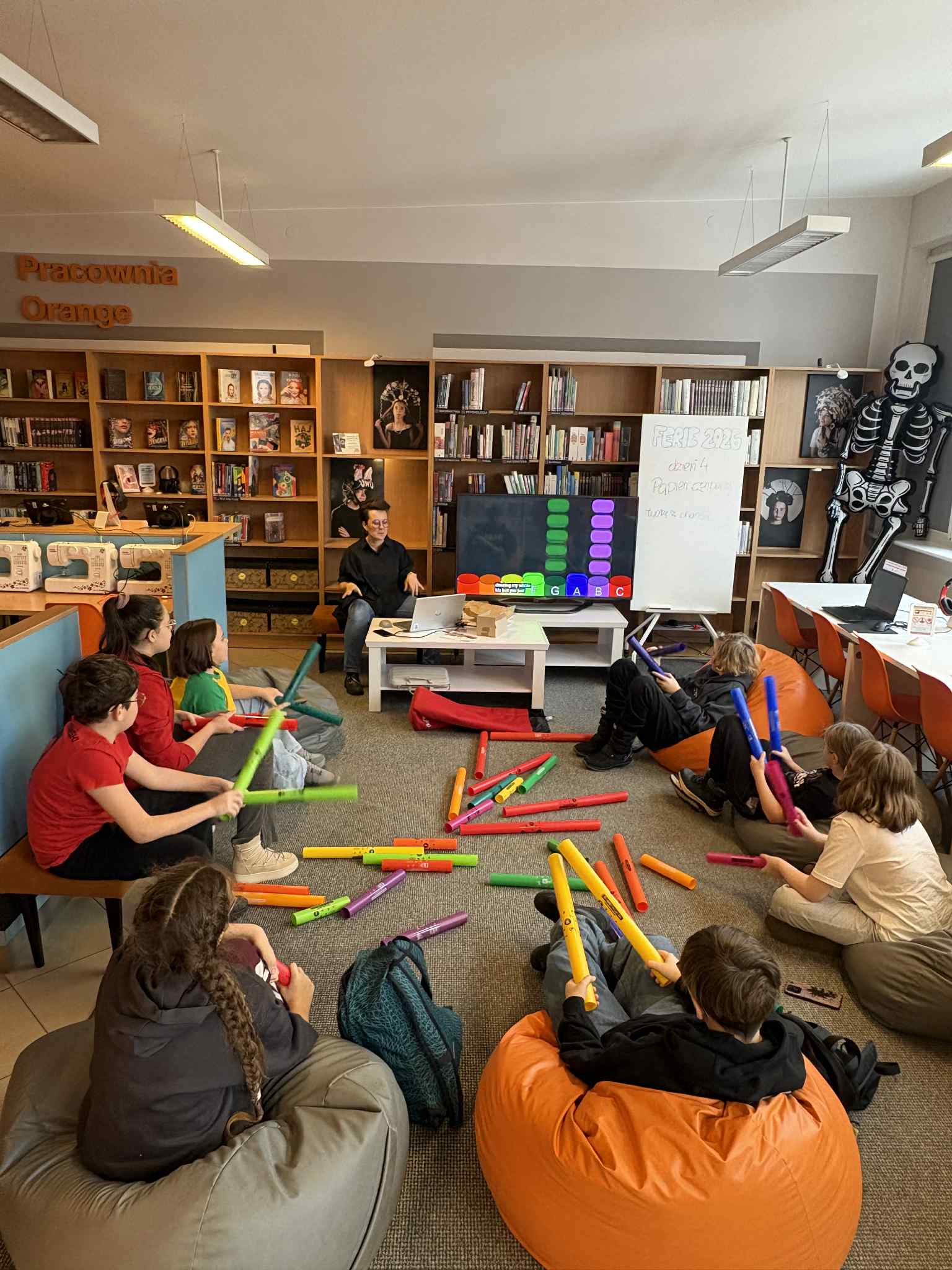 Dzieci siedzą na pufach i grają na kolorowych tubach muzycznych.