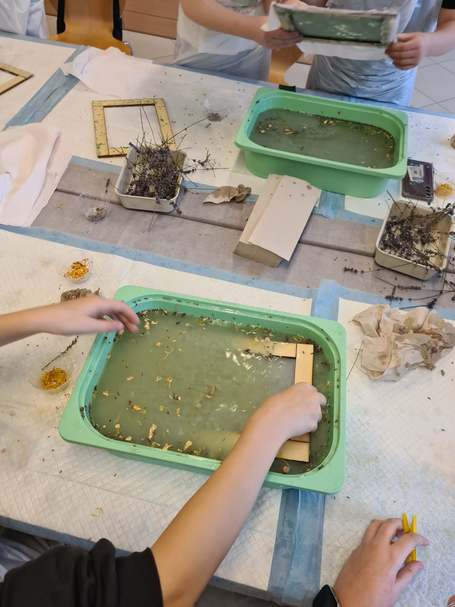 Ręce zanurzają ramę do papieru czerpanego w misce z masą papierową.