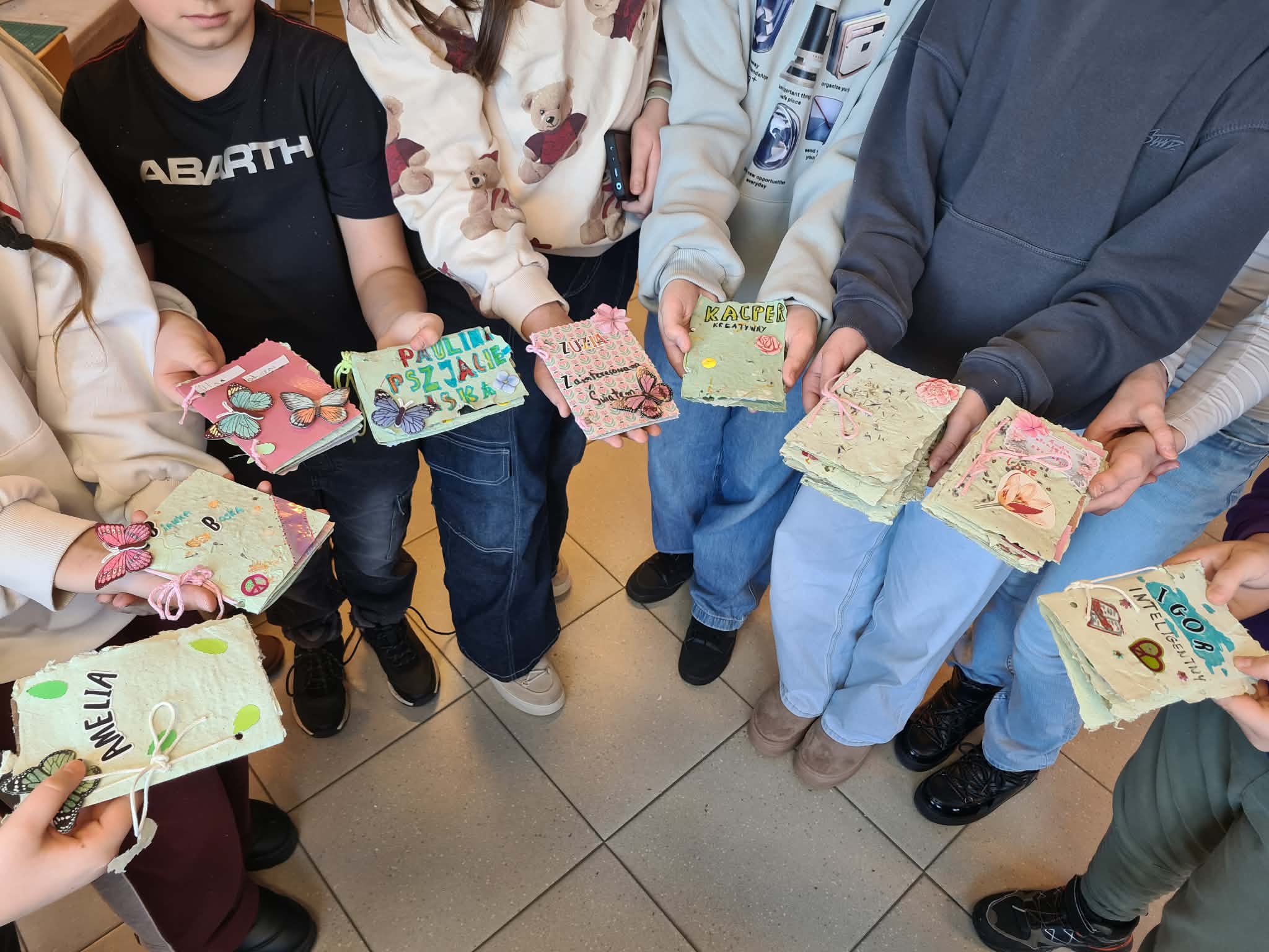 Grupa dzieci trzyma w dłoniach własnoręcznie wykonane książeczki z papieru czerpanego.