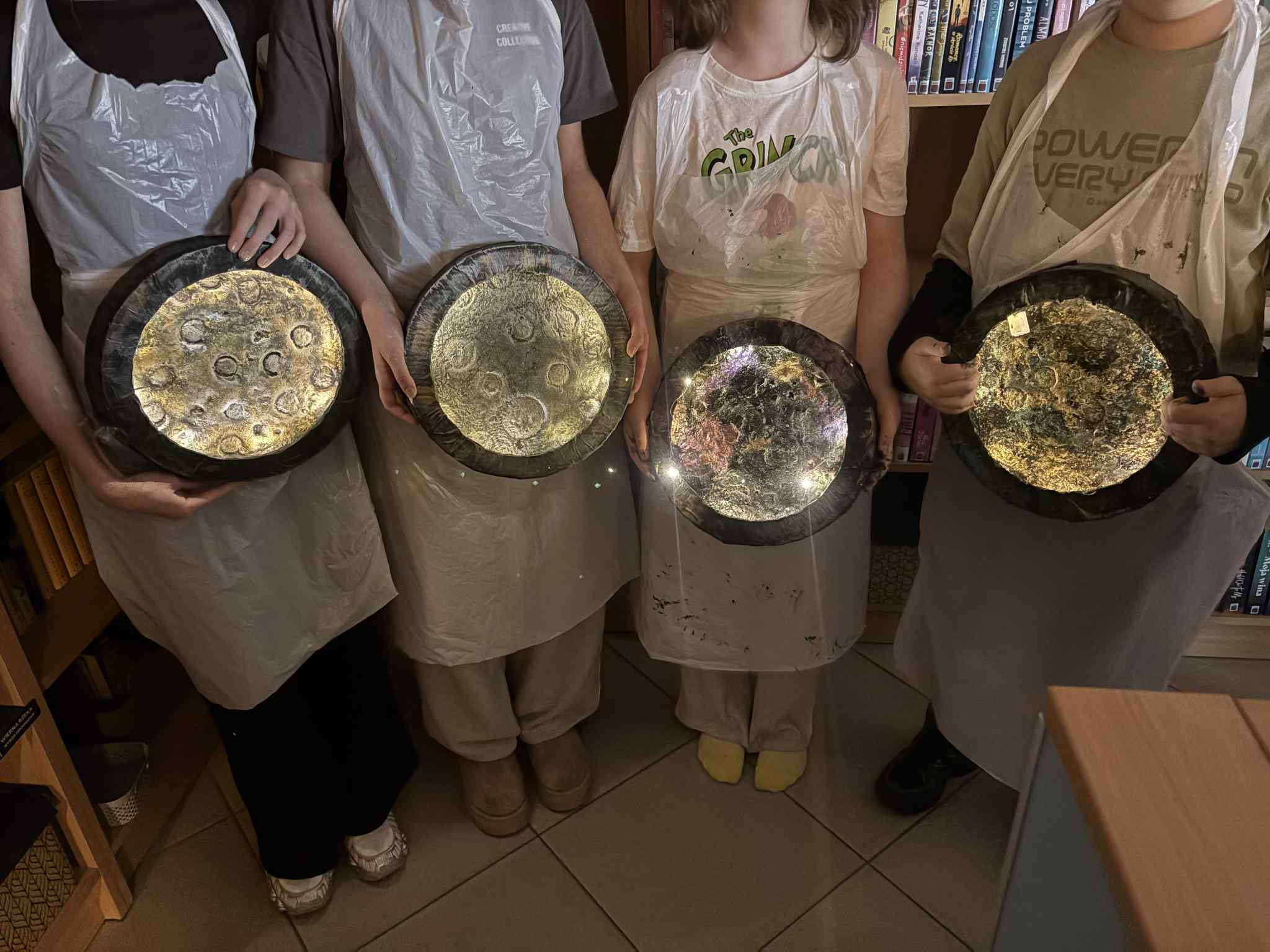 Dzieci stoją obok siebie i trzymają okrągłe, błyszczące prace plastyczne przypominające Księżyc.
