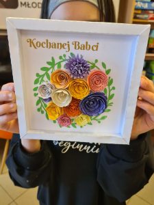 Uczestnik prezentuje gotową pracę – ramkę z przestrzennymi kwiatami z papieru.