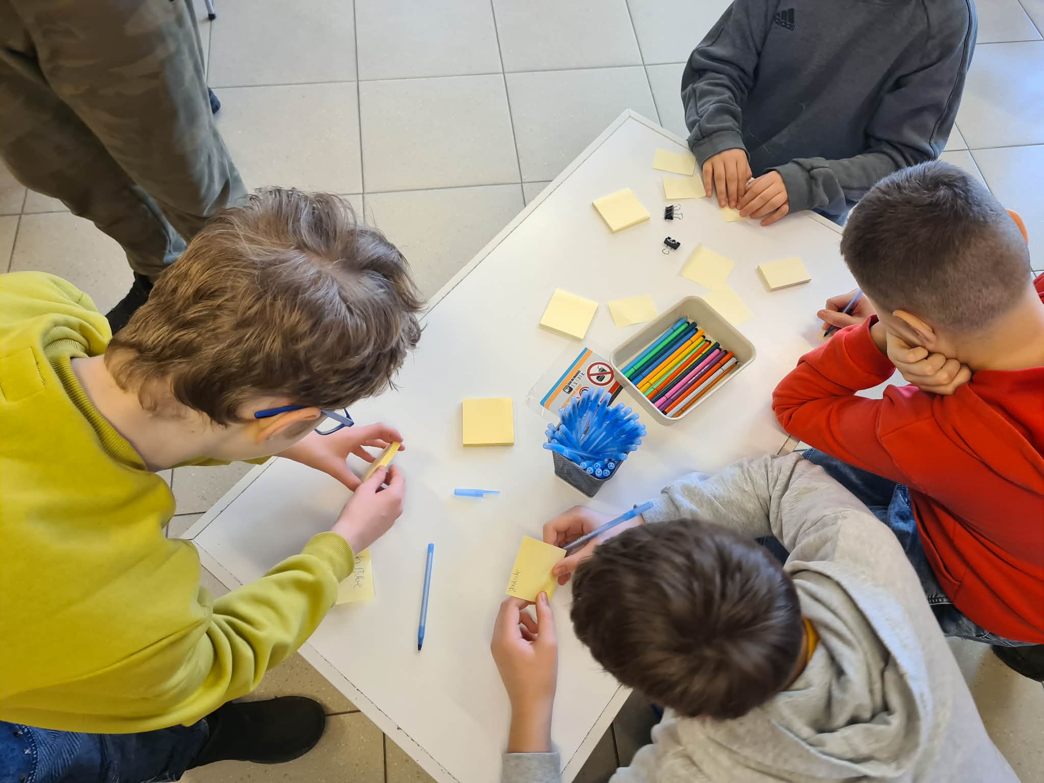Uczniowie zapisują pomysły na żółtych karteczkach przy wspólnym stole.